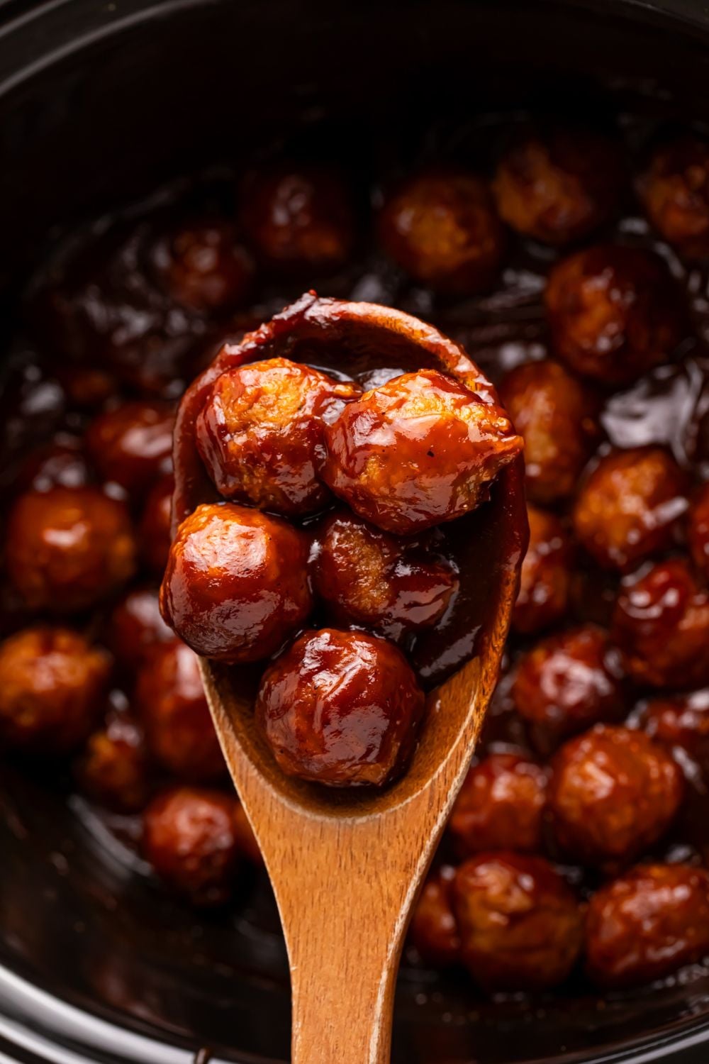 wooden spoon with meatballs with bbq sauce on them sitting over the crockpot