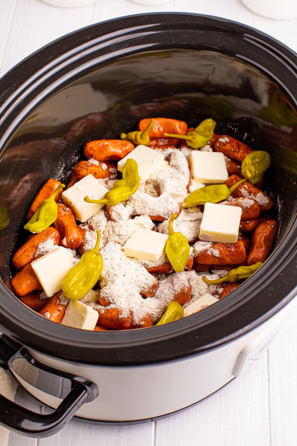 lil smokies in slow cooker with sauce, butter and peppers on top