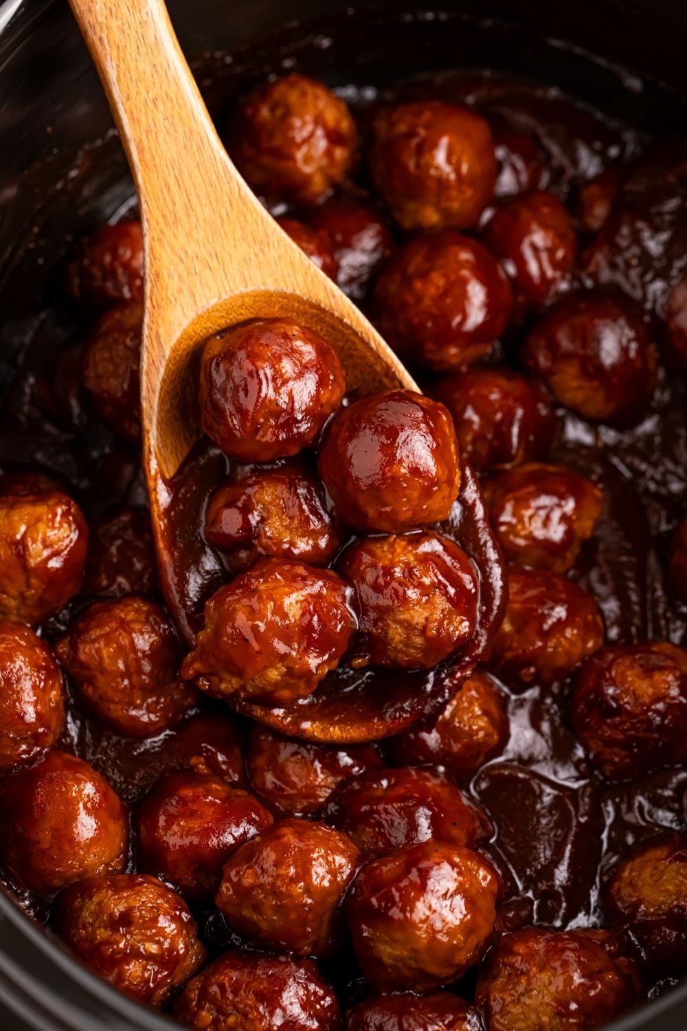 Crockpot Apple Butter Meatballs with a wooden spoon scooping some meatballs out of bowl