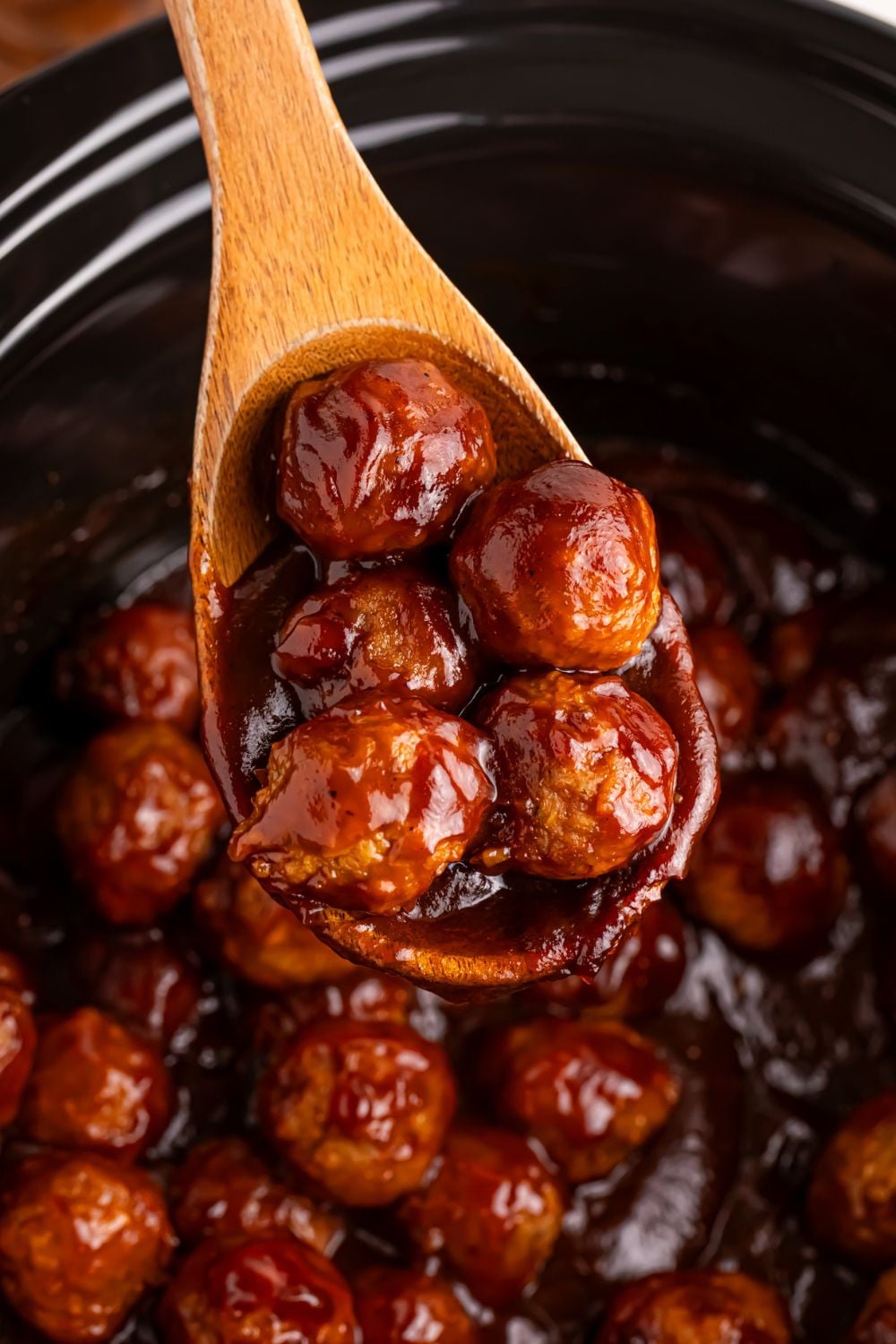wooden spoon with a few meatballs smothered in sauce sitting over a slow cooker