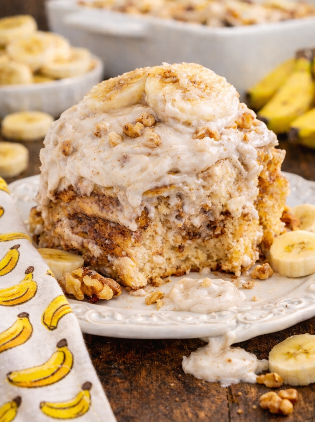 Banana nut cinnamon roll on a white plate with sliced bananas with a bite missing