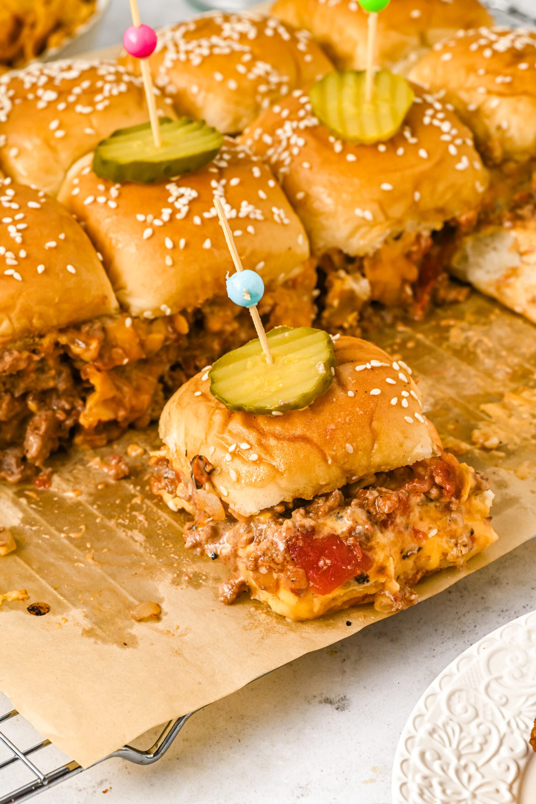 Overhead view of Cheeseburger Sliders on a wire rack garnished with pickle slices.