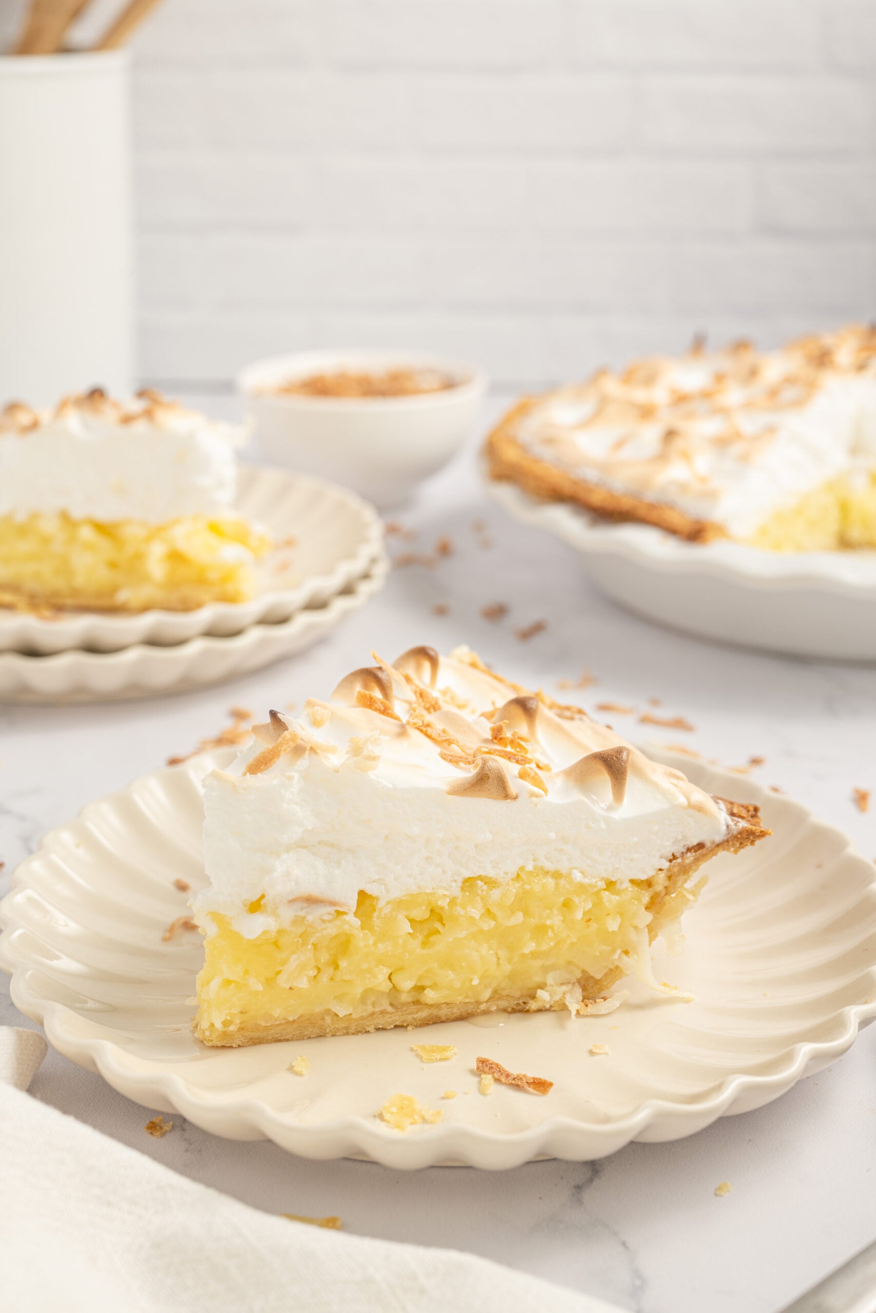 Coconut Meringue Pie on plate with toasted coconut sprinkled around it on table 