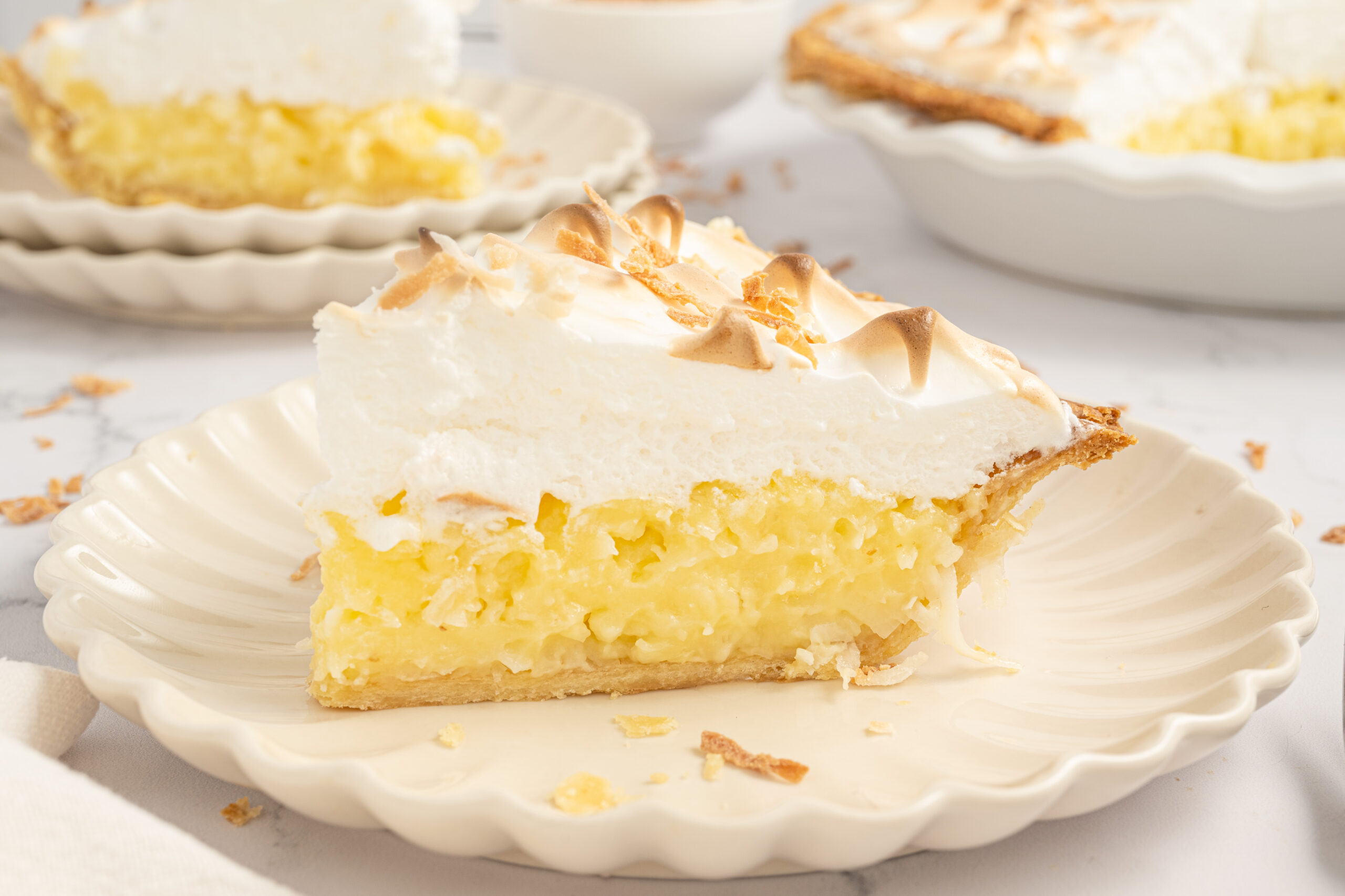 Up close shot of my Coconut Meringue Pie on plate with toasted coconut sprinkled around it on table 