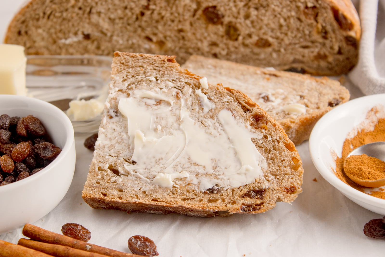 Cinnamon raisin bread on table that is half sliced into slices with one slathered with butter