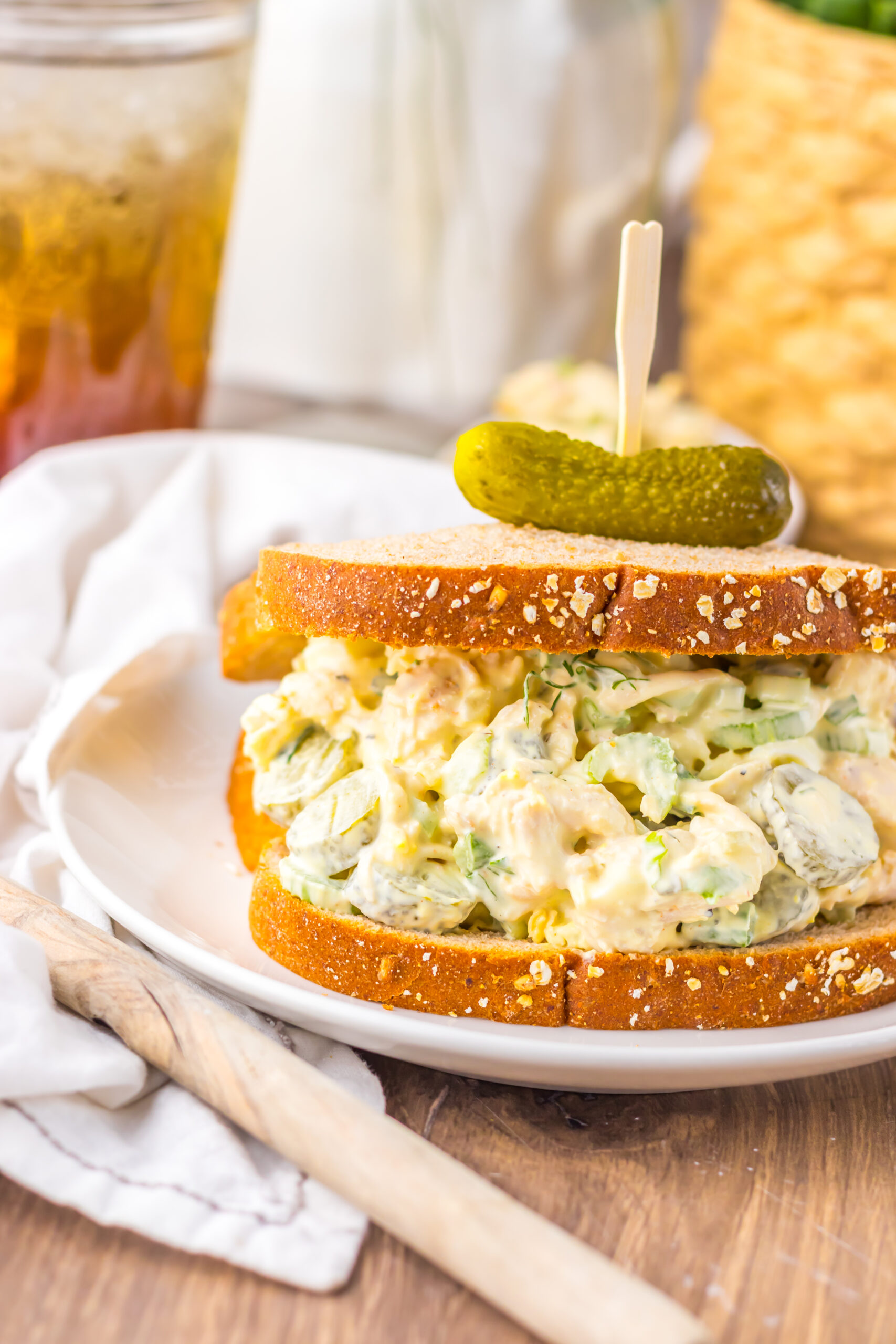 Pickle Chicken Salad sandwich on a white plate topped with a tiny pickle