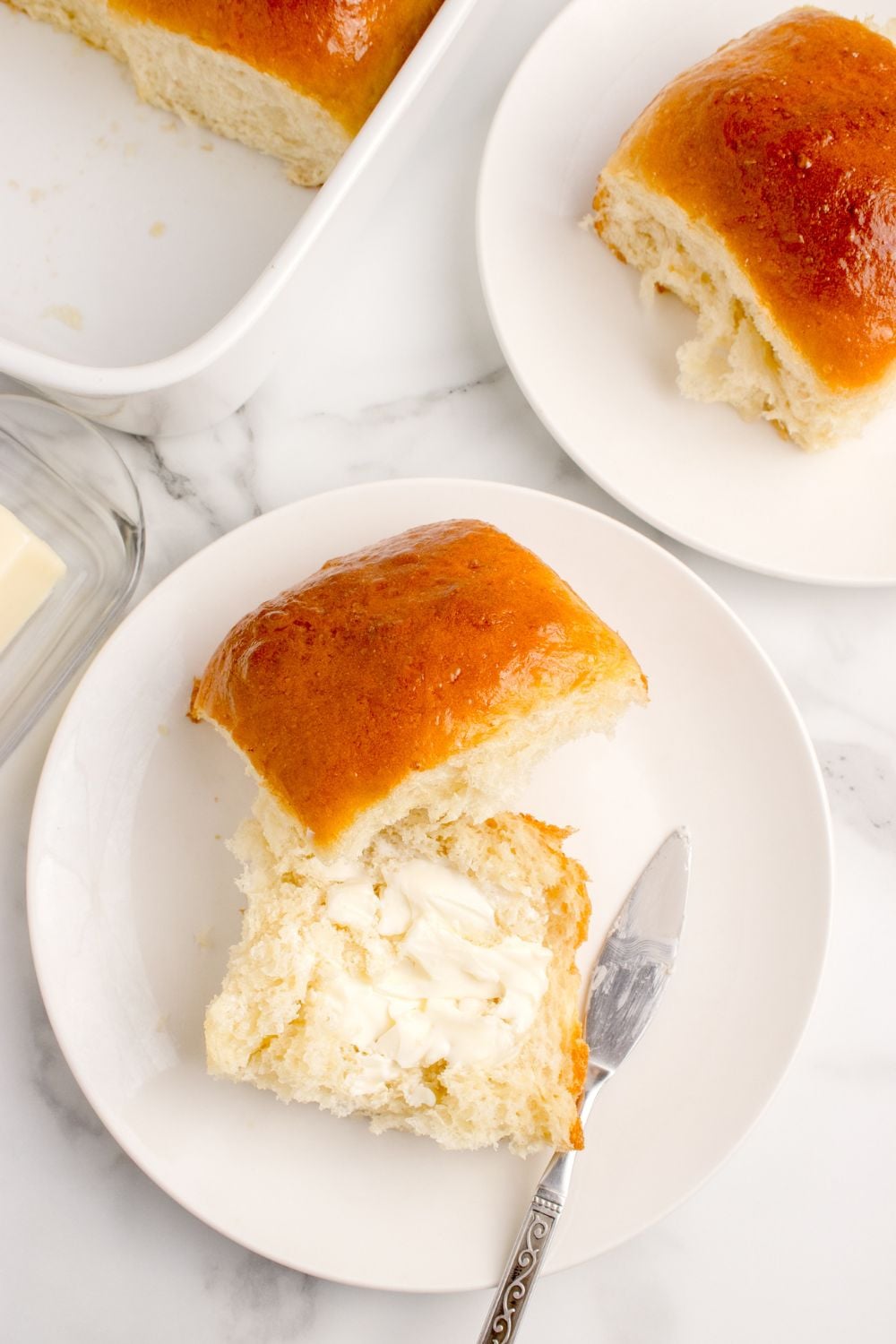 Pull Apart Dinner Rolls on plates with one cut in half and buttered