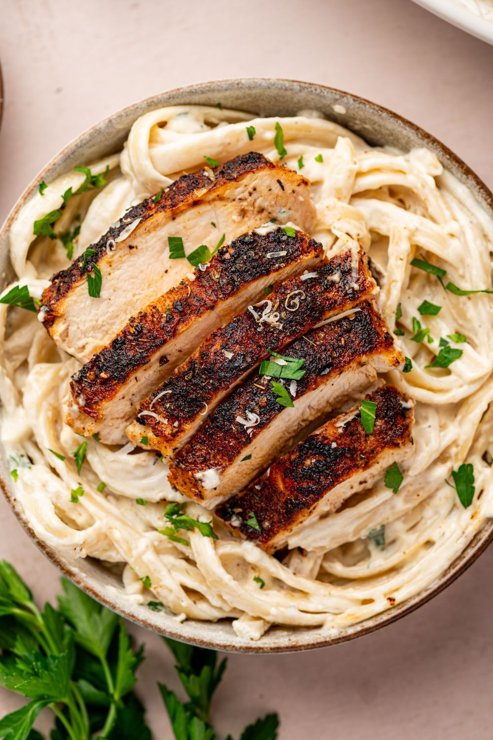 Blackened Chicken Alfredo in a bowl with parsley and parmesan grated on top of bowl 