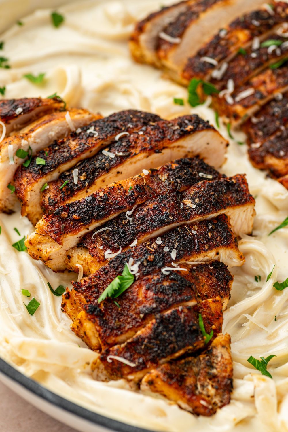 Blackened Chicken Alfredo in a bowl with a close up look of chicken on top of pasta 