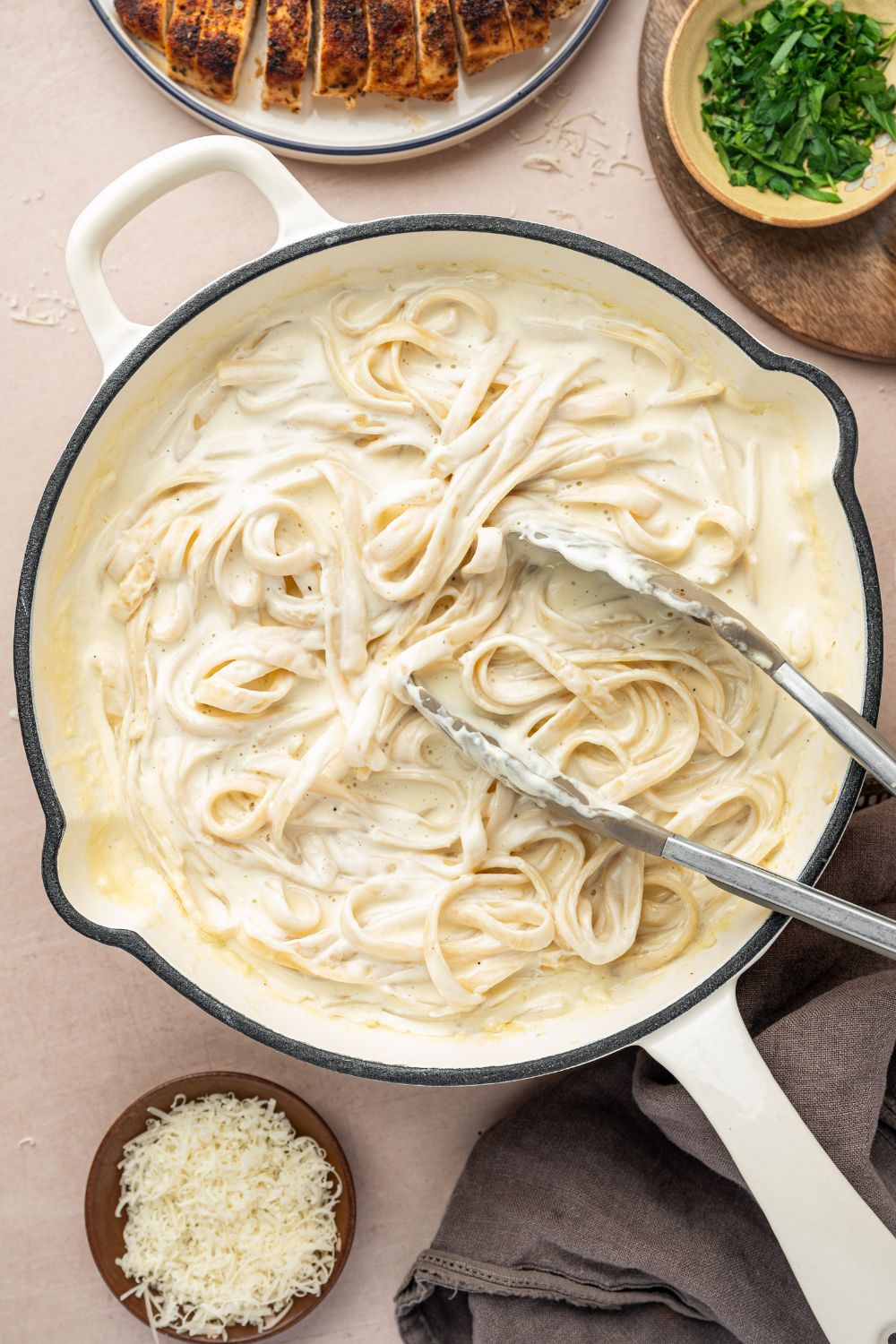 alfredo noodles in a skillet with tongs sitting on top of the pasta 