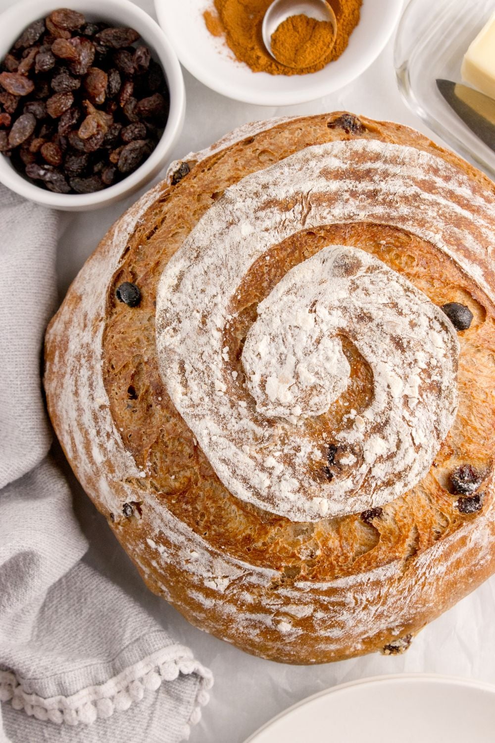 round loaf of cinnamon raisin bread on table with a bowl of raisins behind it