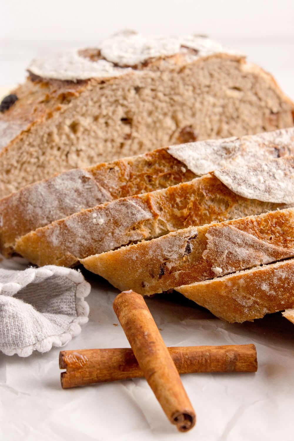cinnamon raisin dutch oven bread sliced and placed on table with two cinnamon sticks sitting in front of loaf