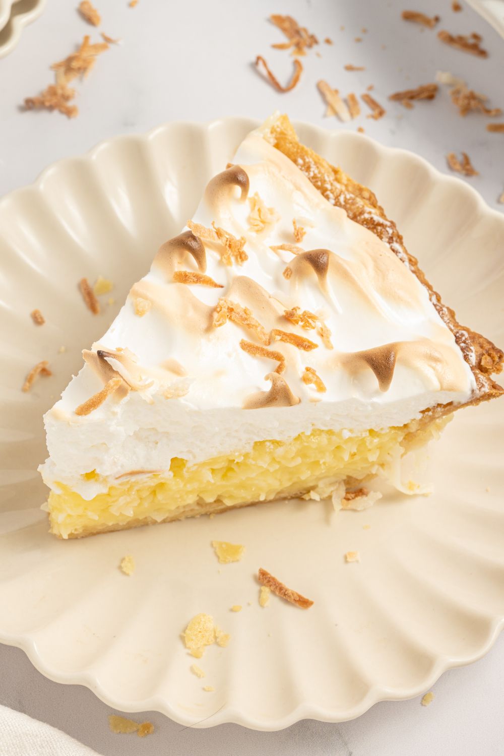 Coconut Meringue Pie on plate with toasted coconut sprinkled around it on table 