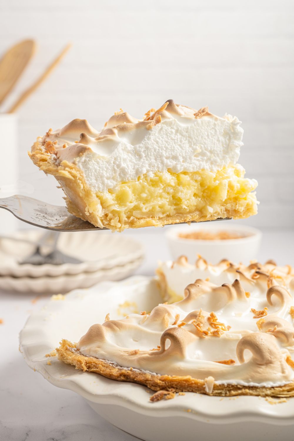 Coconut Meringue Pie in pie plate with a slice lifting out of the pie plate 