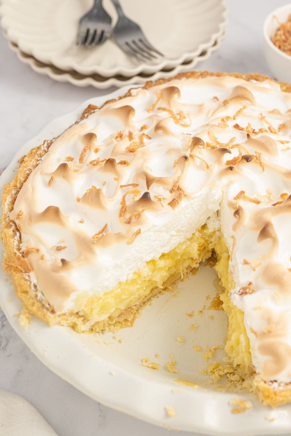 Coconut Meringue Pie in a pie plate with one slice taken out so you can see the filling and meringue layers 