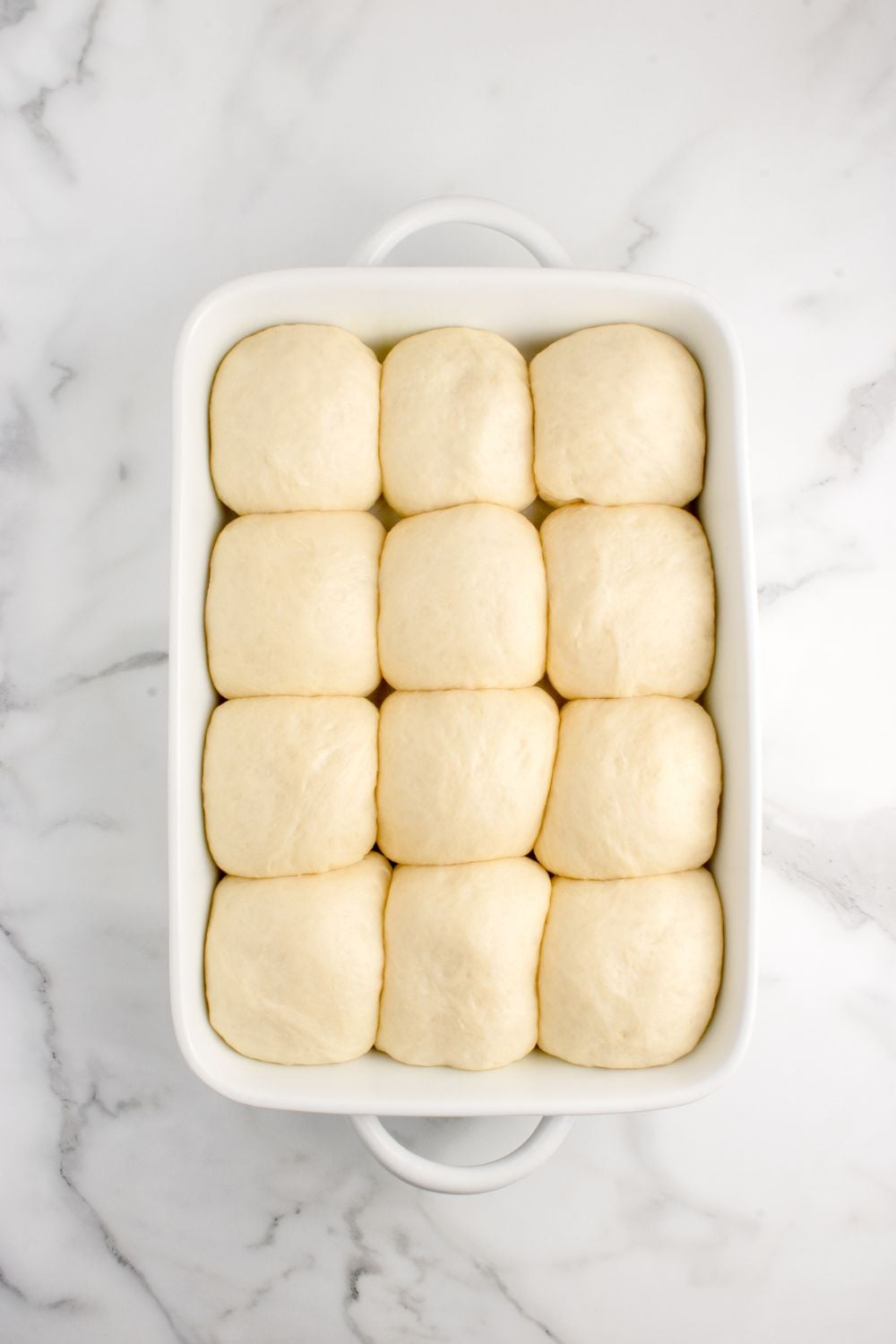 risen dough for rolls in a casserole dish on table