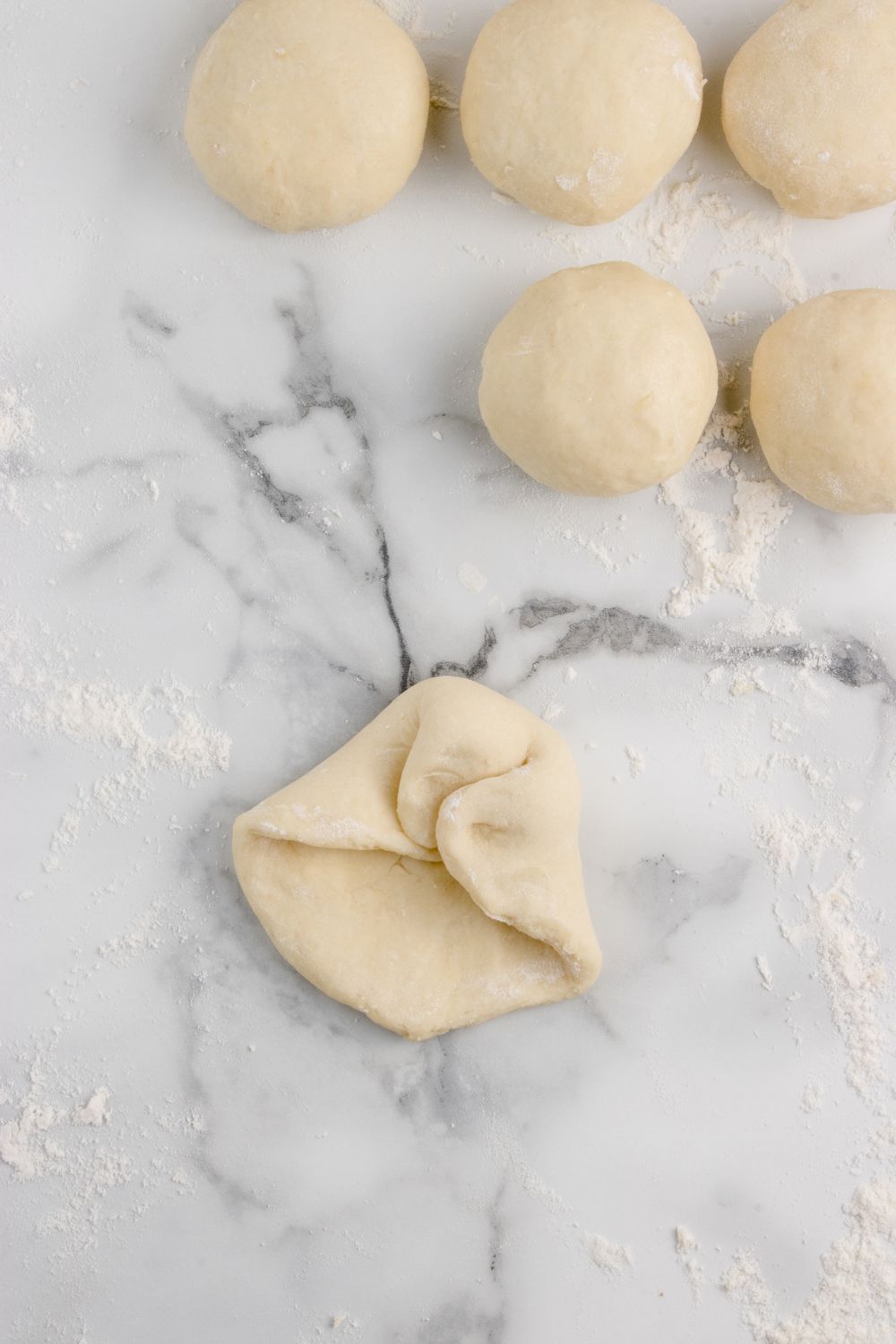 folding up bread dough in balls for making Hawaiian rolls