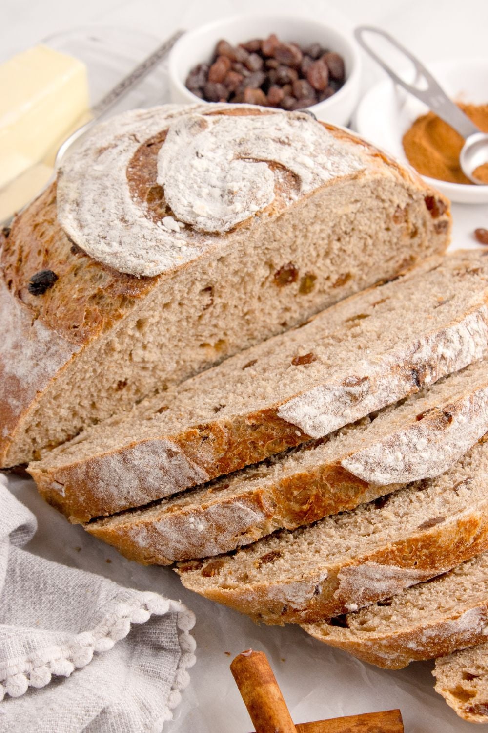 homemade cinnamon raisin bread partly sliced and sitting on table with some raisins in a bowl behind it