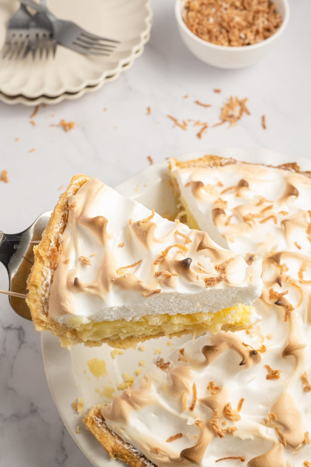 Coconut Meringue Pie on table with one slice being lifted from the pie plate 