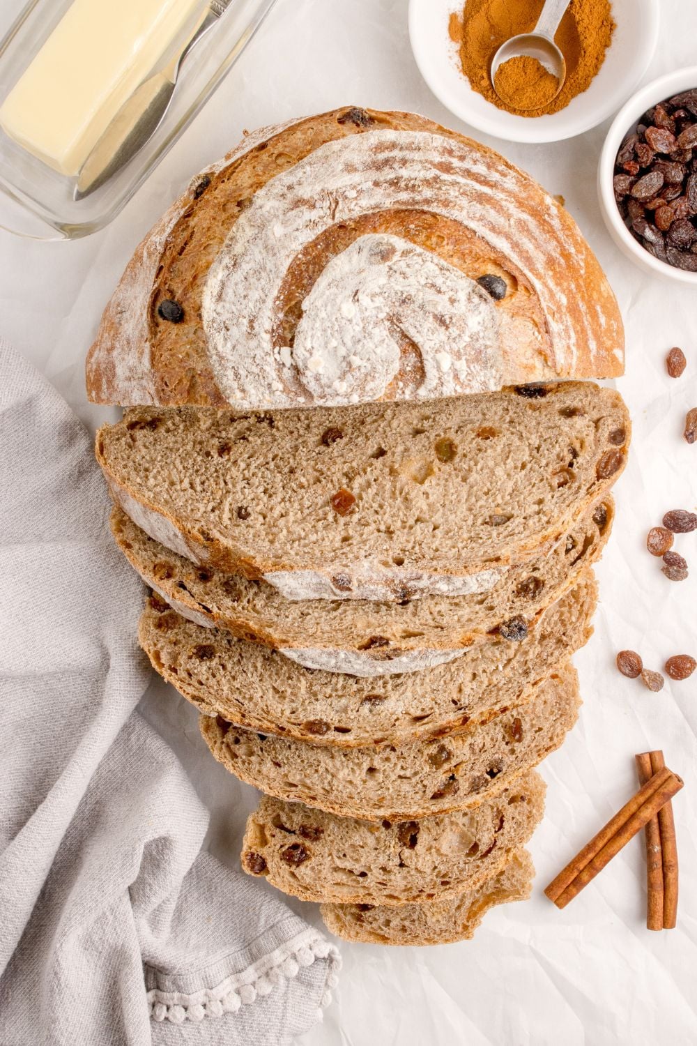 no knead raisin bread sliced and placed on table with cinnamon sticks and raisins around the loaf of bread