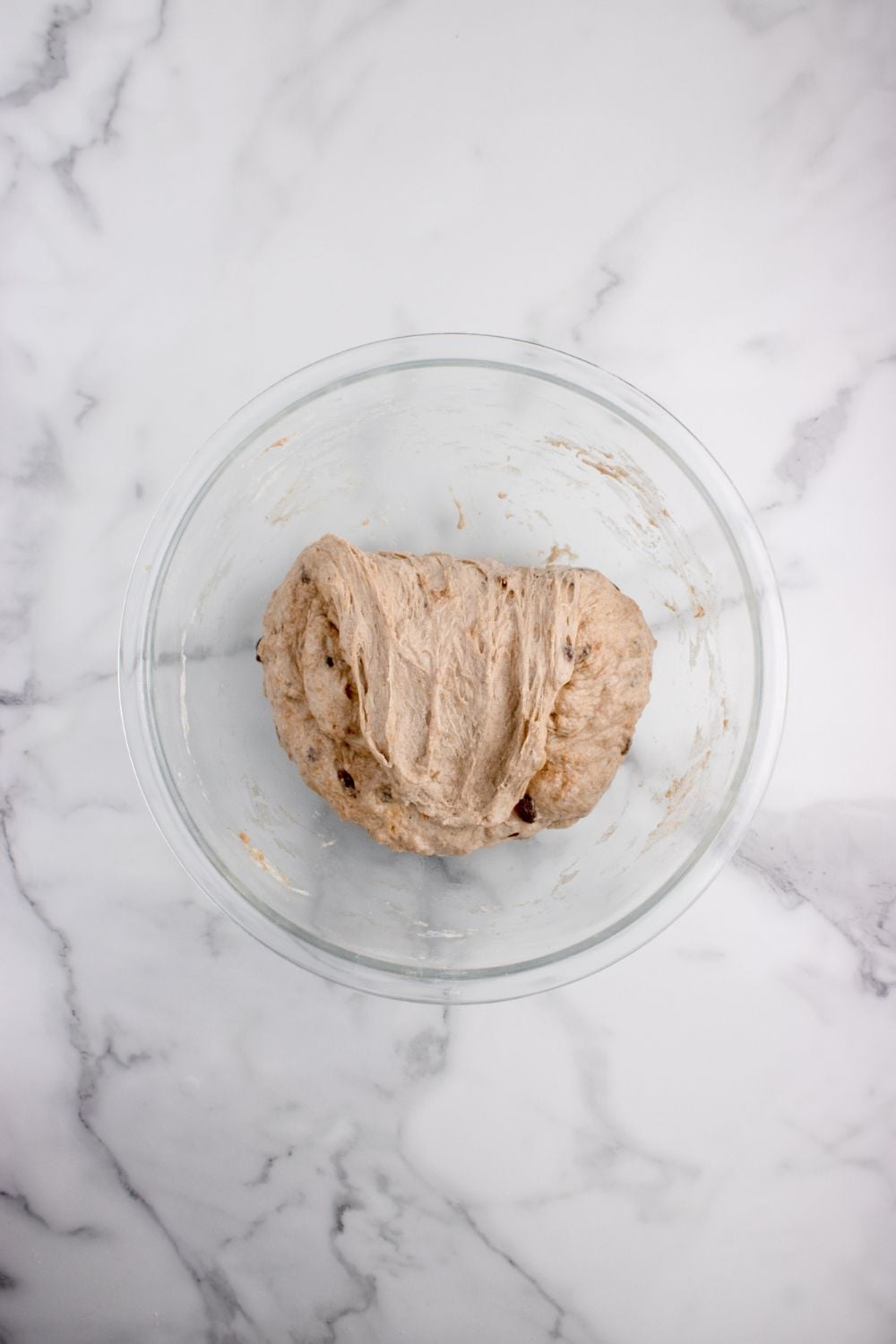 dough of cinnamon raisin bread in a glass bowl on table