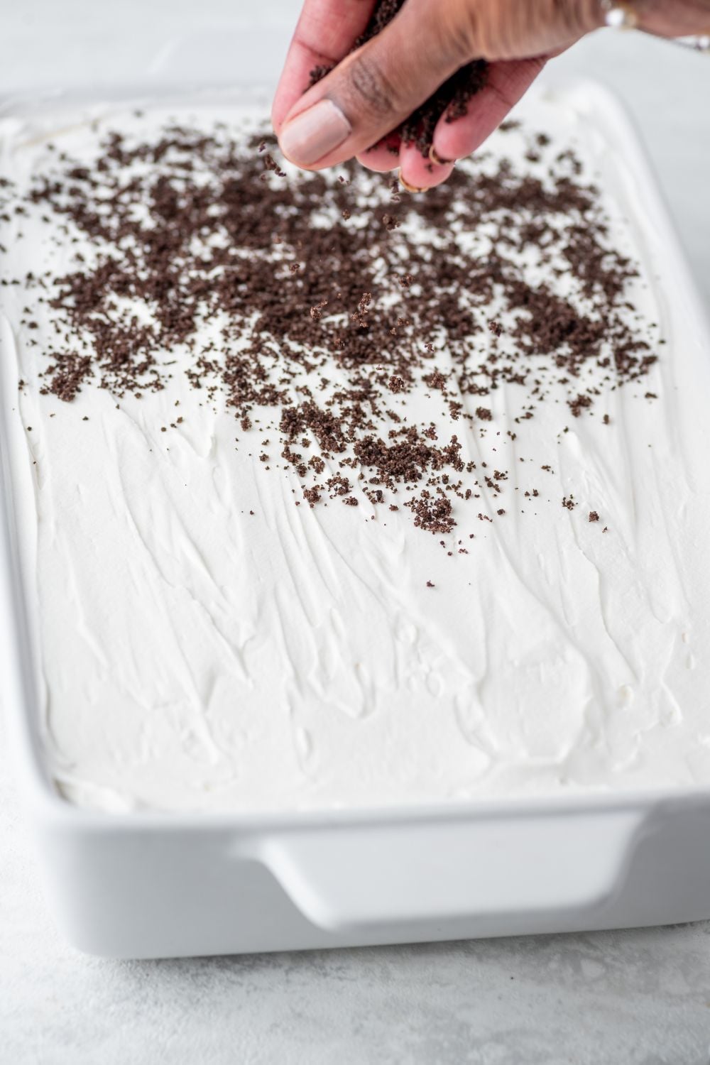 sprinkling crushed cookies on top of the Chocolate Oreo Lush in pan 