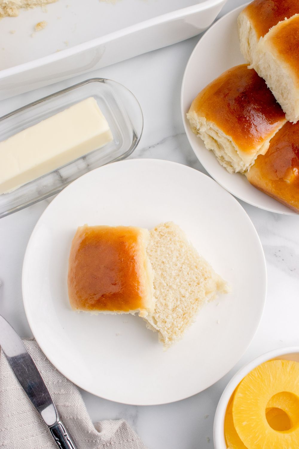 plate of dinner rolls on table, and a slice of bread on plate with a stick of butter on side