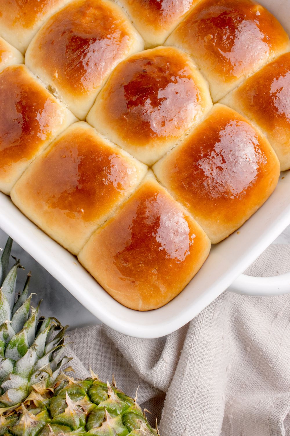 sweet hawaiian rolls in a pan on table with a pineapple on side of table