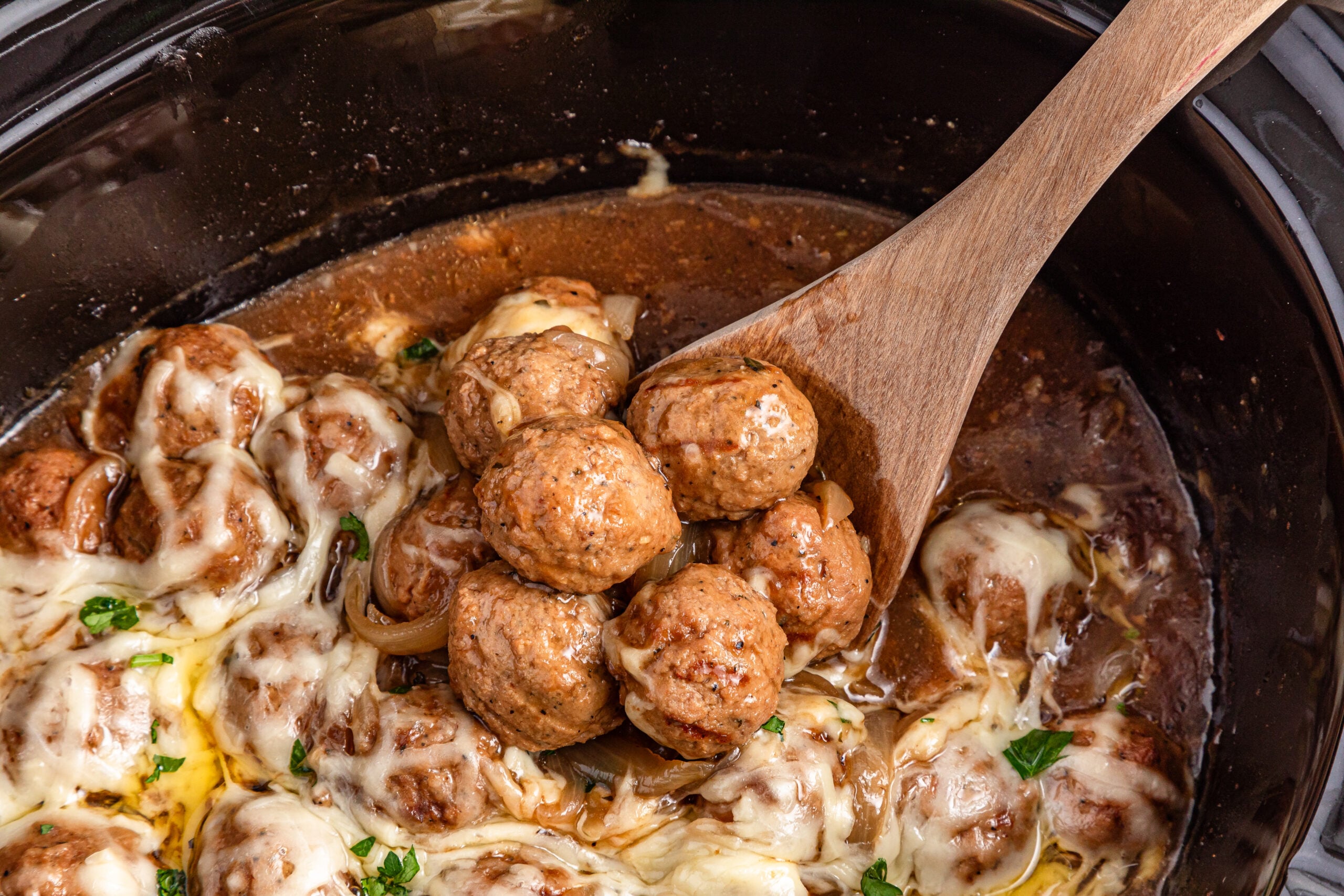 Crock Pot French Onion Meatballs with some being scooped out of slow cooker with spoon