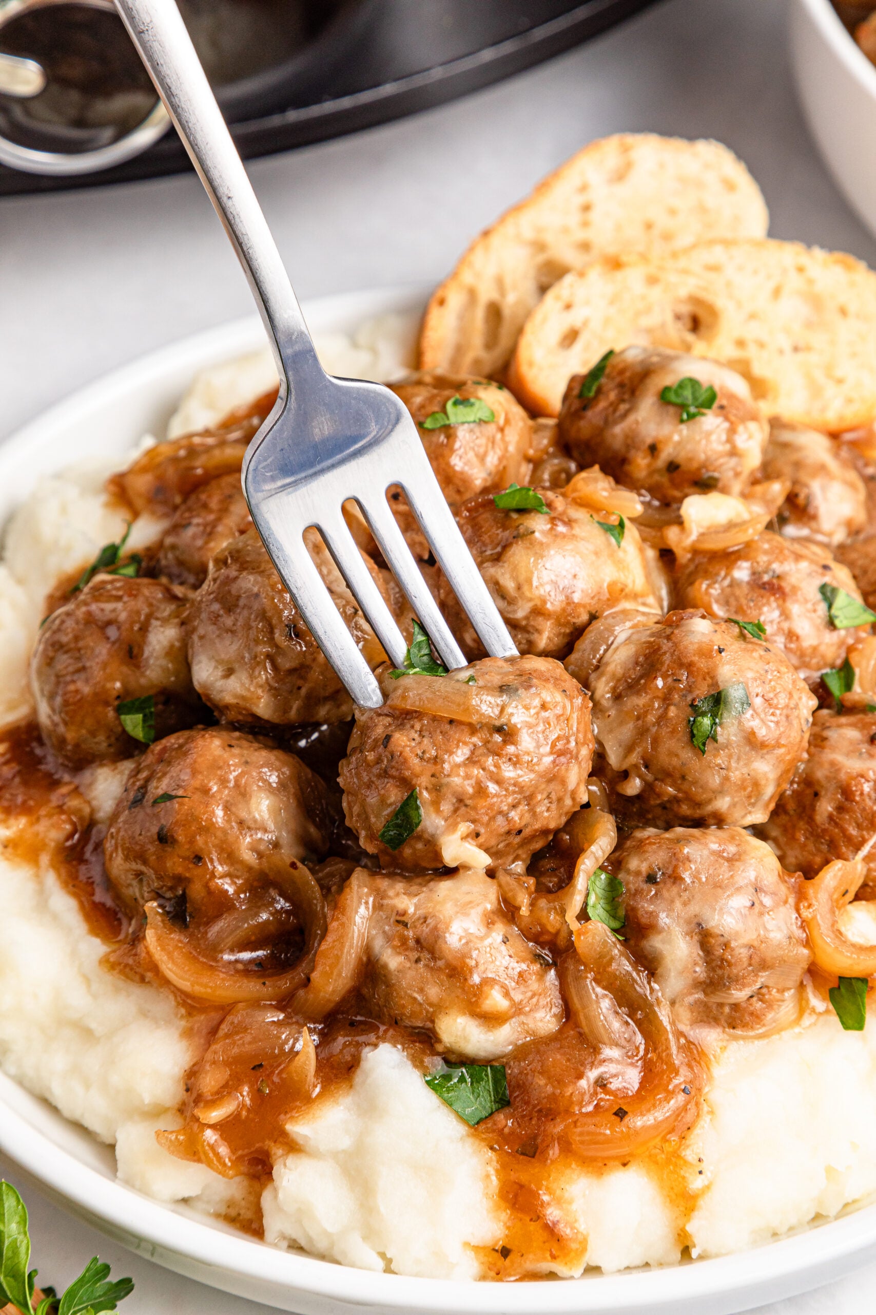 Crock Pot French Onion Meatballs in a white plate with a fork lifting one up