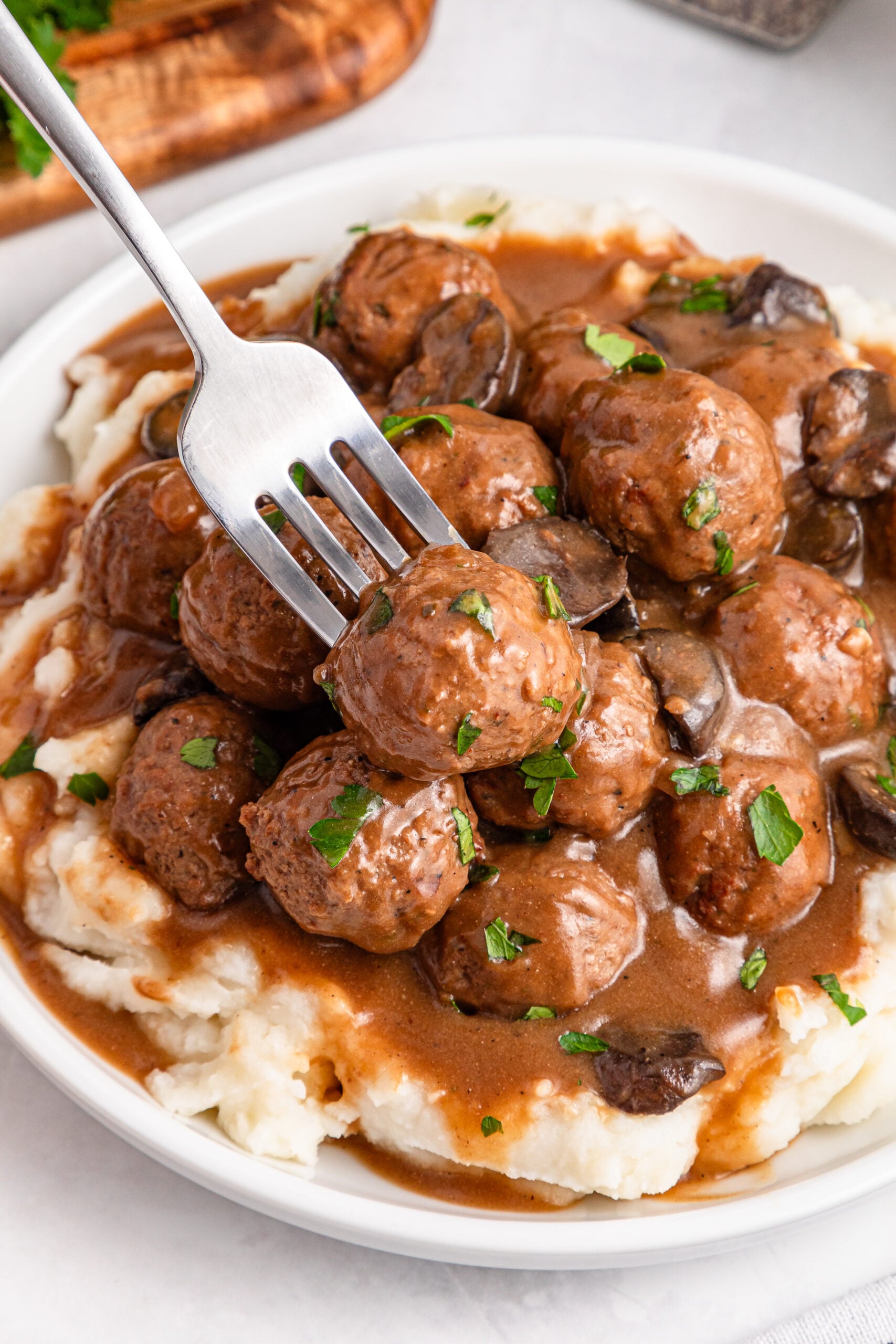 Crock Pot Salisbury Steak Meatballs on a plate with mashed potatoes under them with a fork on the side