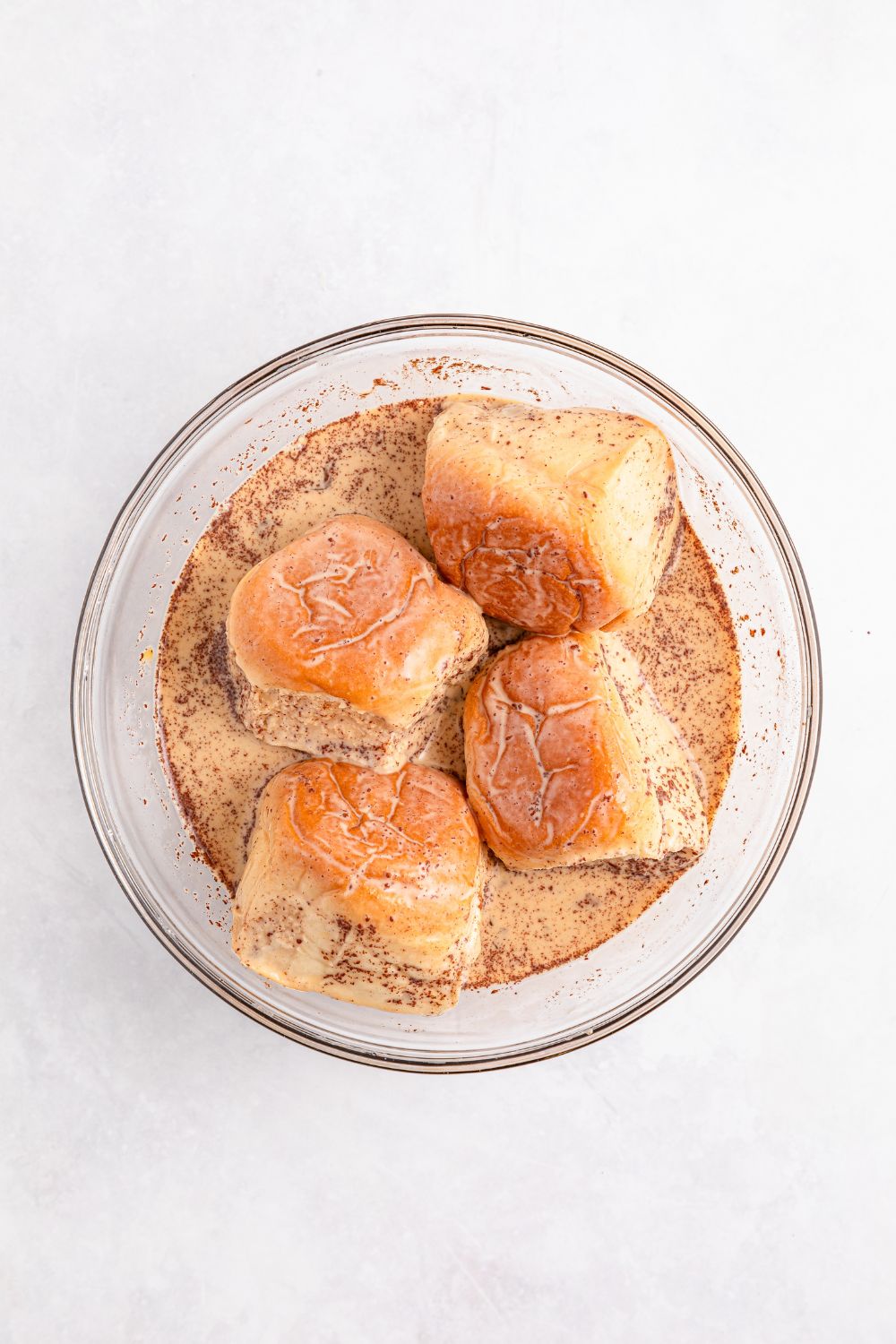 Hawaiian sweet rolls soaking in a French toast mixture in a glass bowl on table 