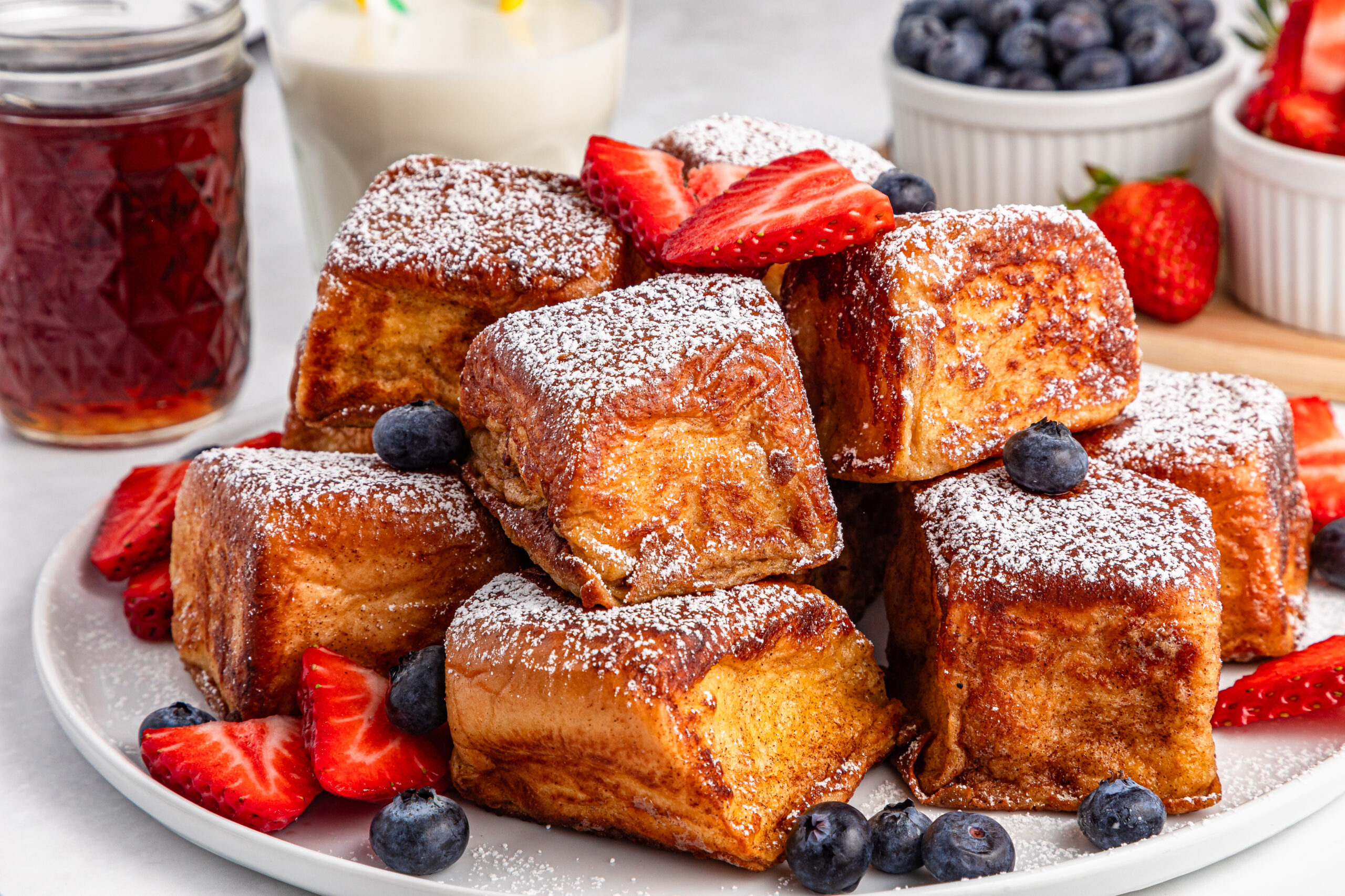 white plate full of the Hawaiian Roll French Toast topped with sliced strawberries and blueberries 