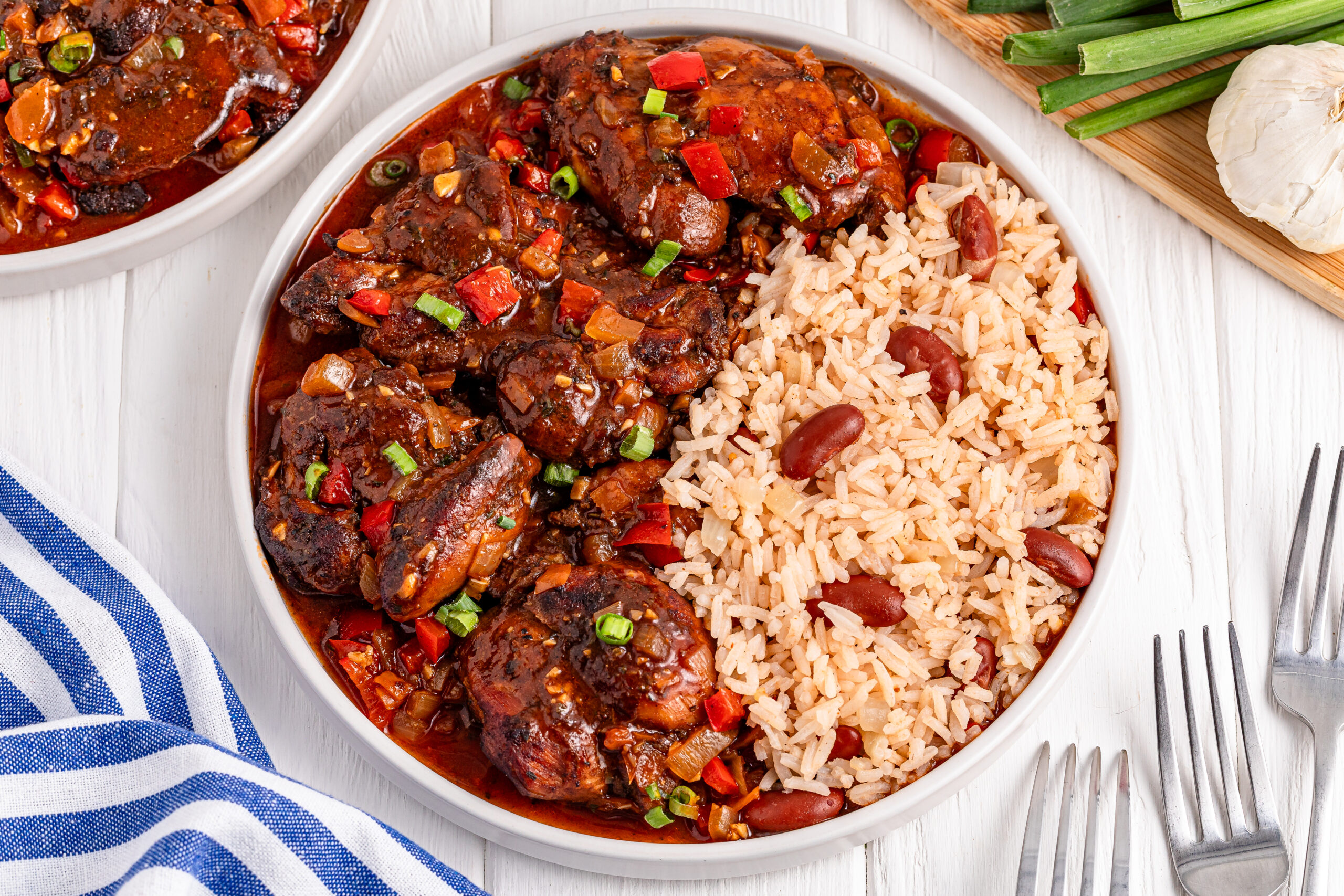 Jamaican Brown Stew Chicken in a white bowl with a side of rice and beans