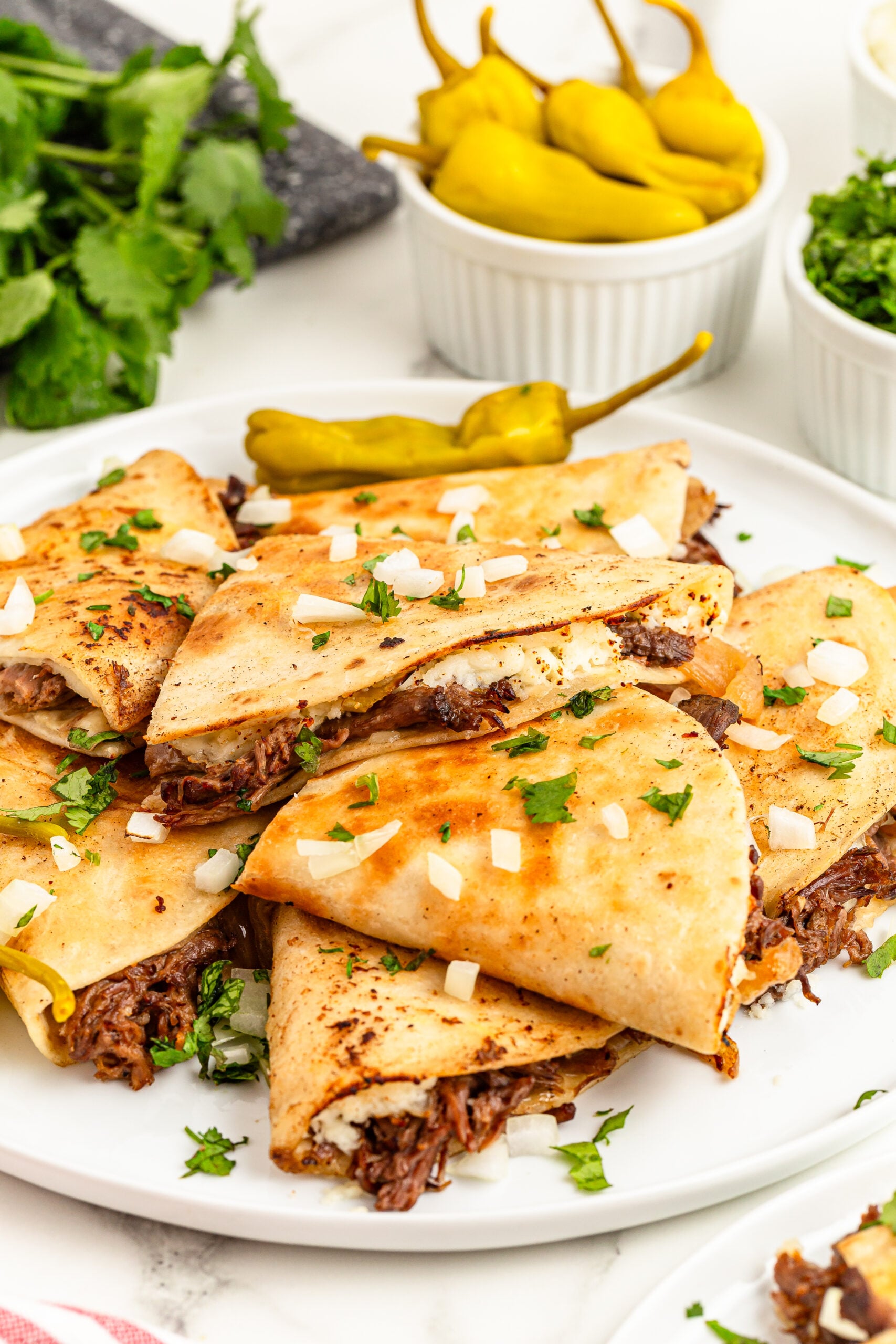 Mississippi Pot Roast Quesadillas piled on a plate with a bowl of peppers in the background