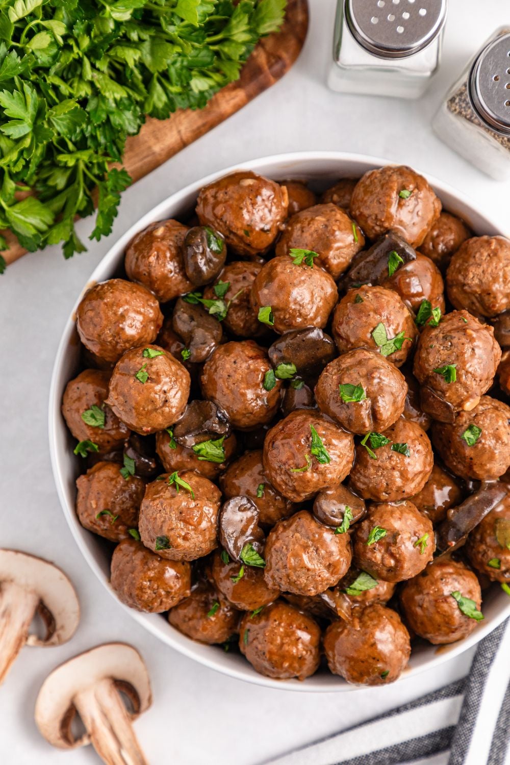 Crock Pot Salisbury Steak Meatballs in a bowl on table with parsley and fresh mushrooms by the bowl on table