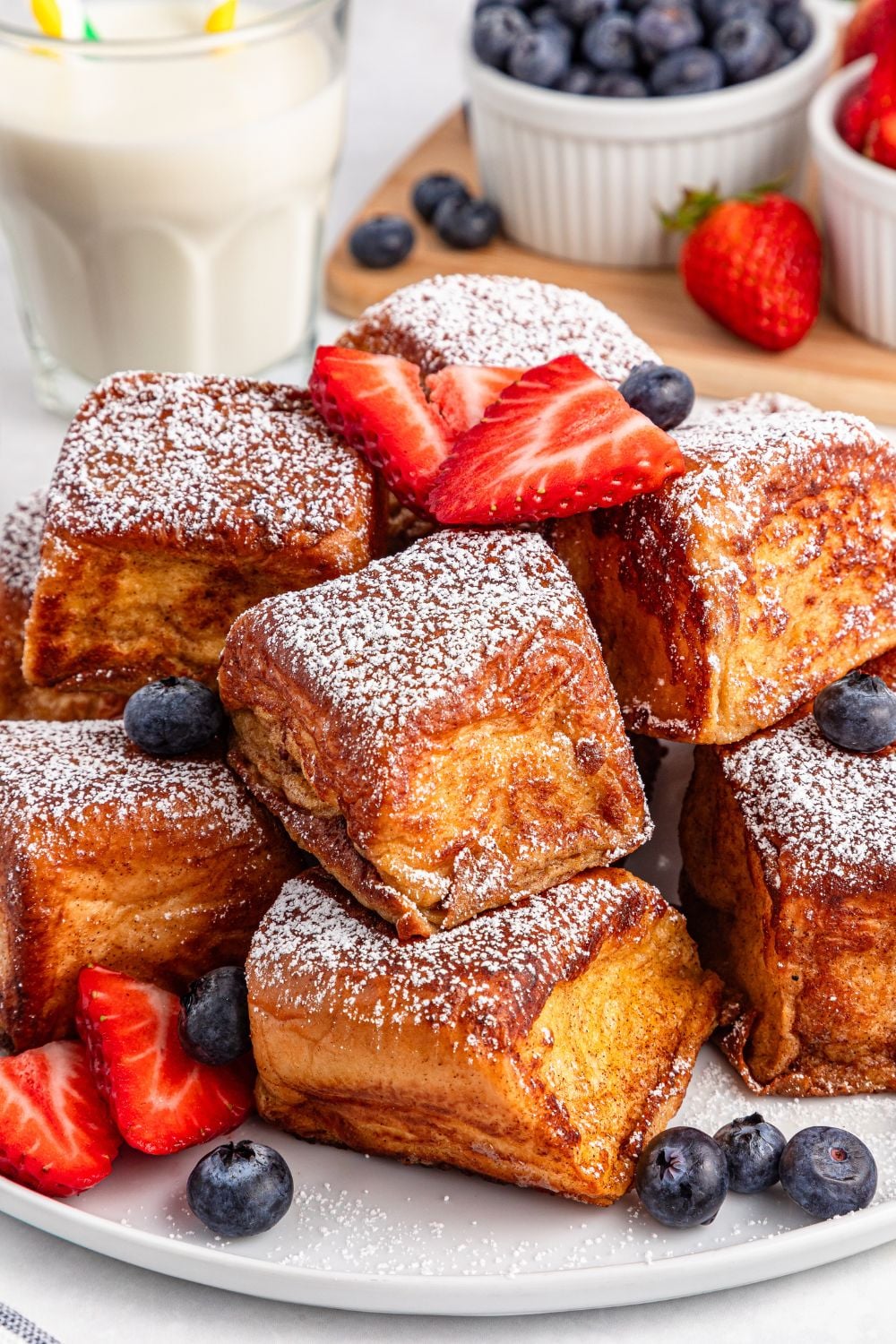 Hawaiian Roll French Toasts stacked on a plate with fruit around it 