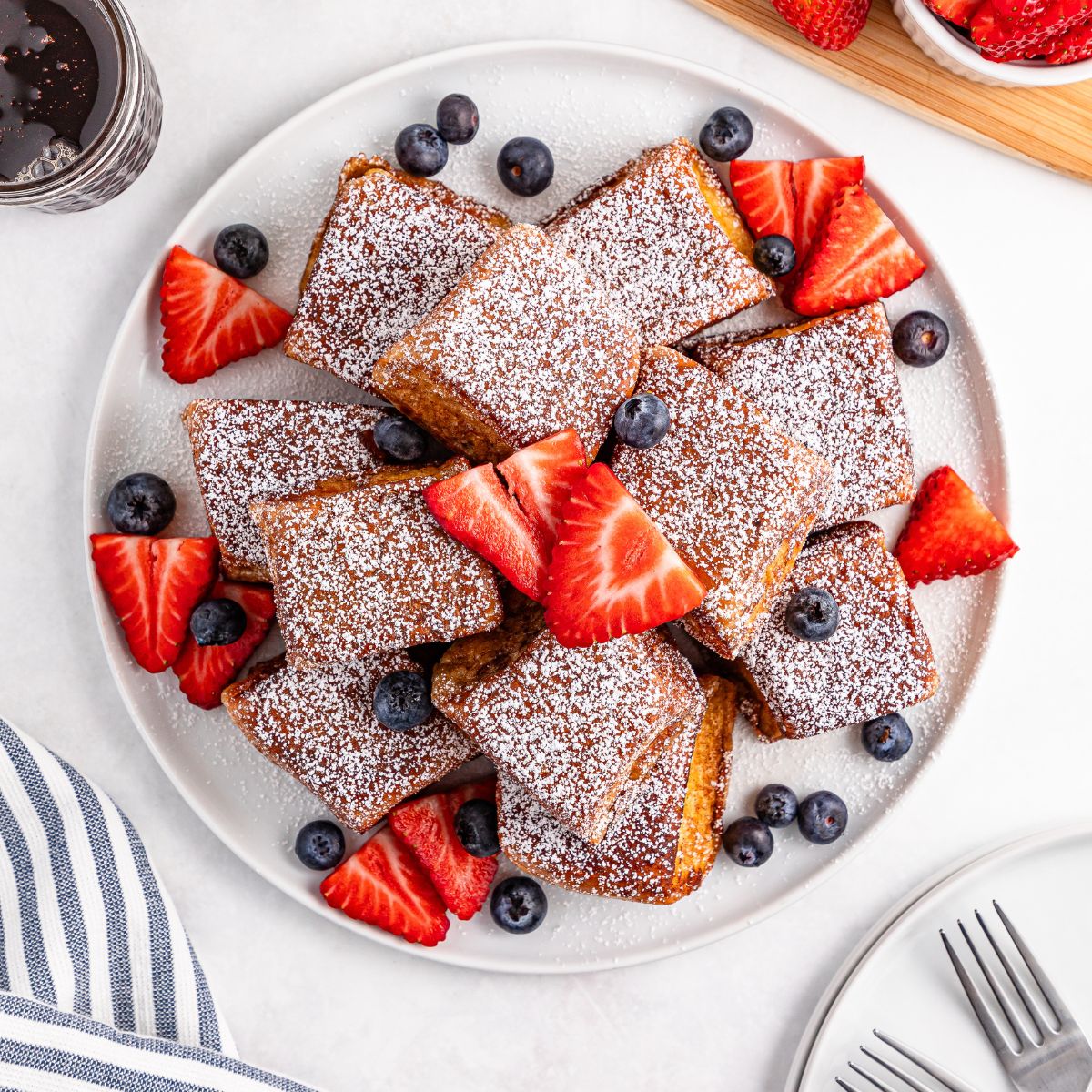 Hawaiian Roll French Toast stacked on a plate with powdered sugar and fruit on top of the French toast