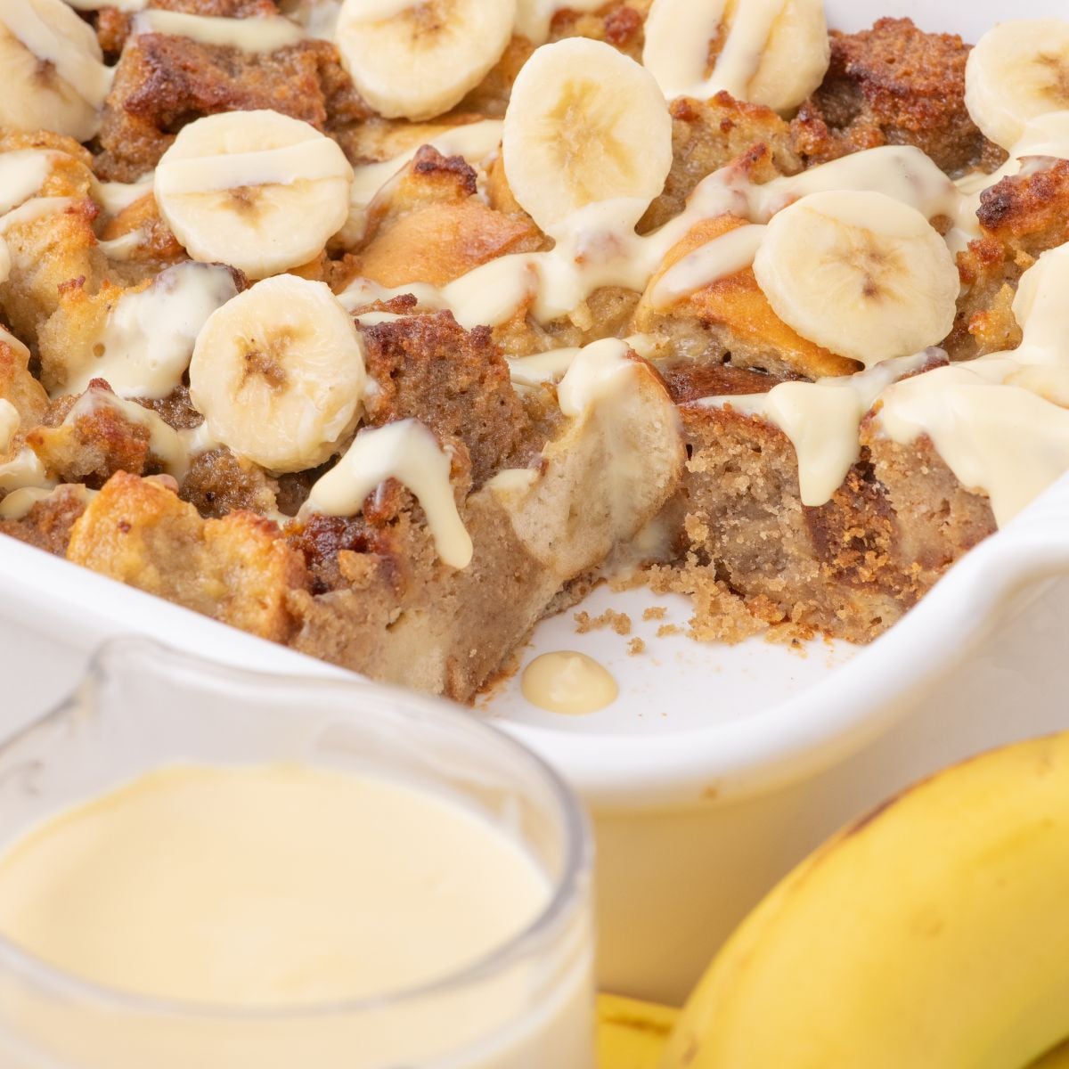 Banana Bread Pudding in a casserole dish with a glass of milk and bananas in front of the pan
