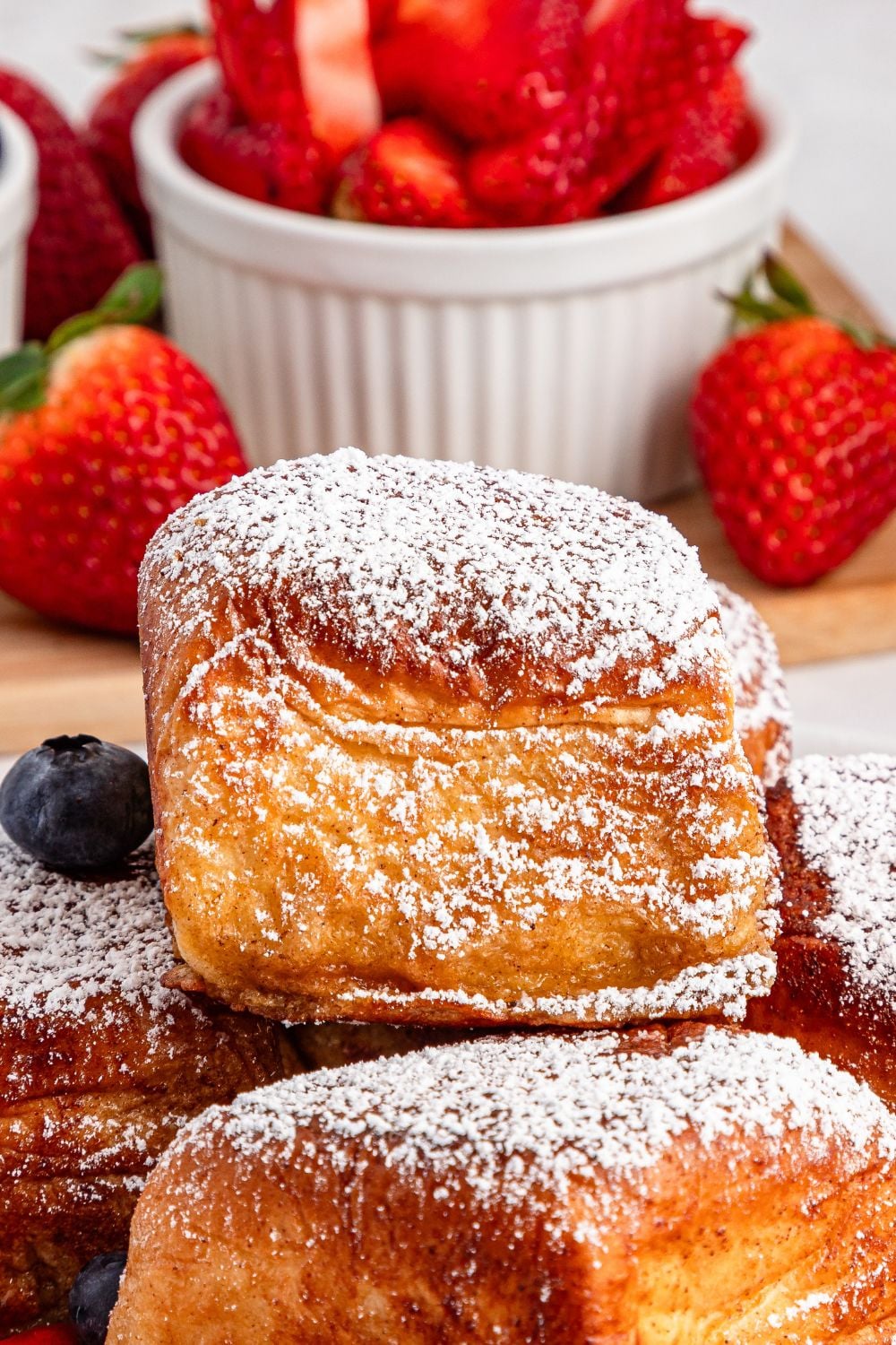 close up of Hawaiian Roll French Toast on a plate with sliced strawberries in a bowl behind it 