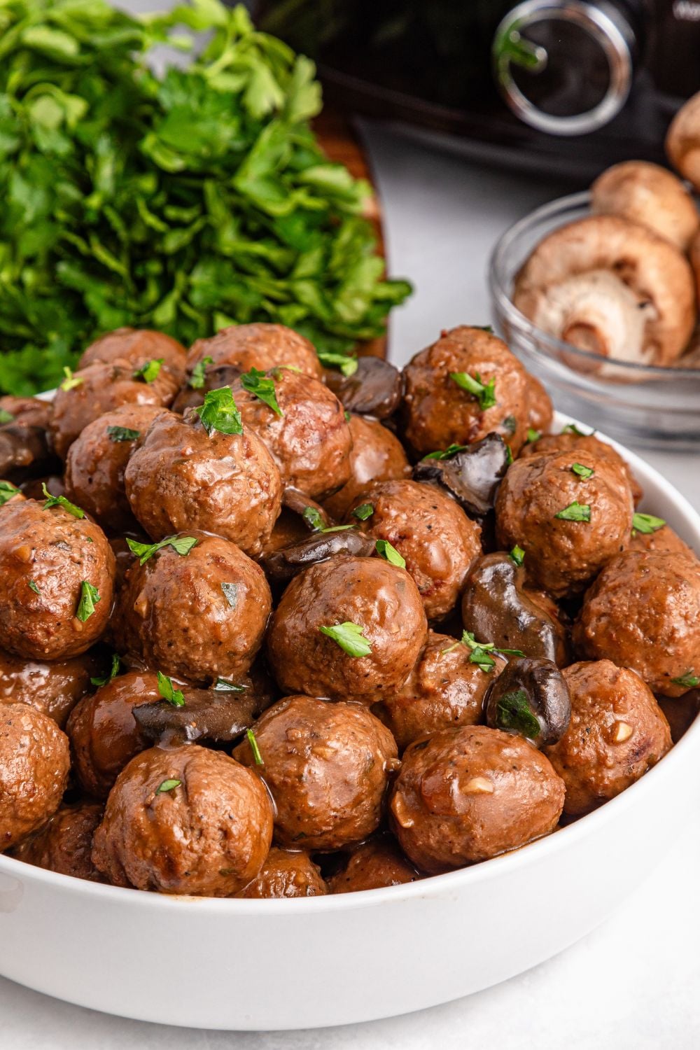 white bowl with Salisbury Steak Meatballs in it and a bunch of parsley in a bundle behind bowl and mushrooms to the side