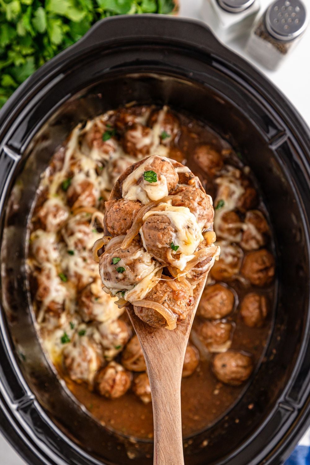 Crock Pot French Onion Meatballs with some being scooped out of slow cooker with spoon