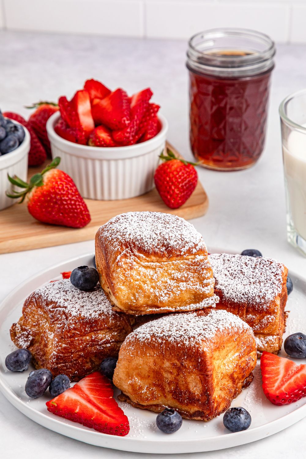 Hawaiian Roll French Toast stacked on plate with berries, and a bowl of strawberries behind it 