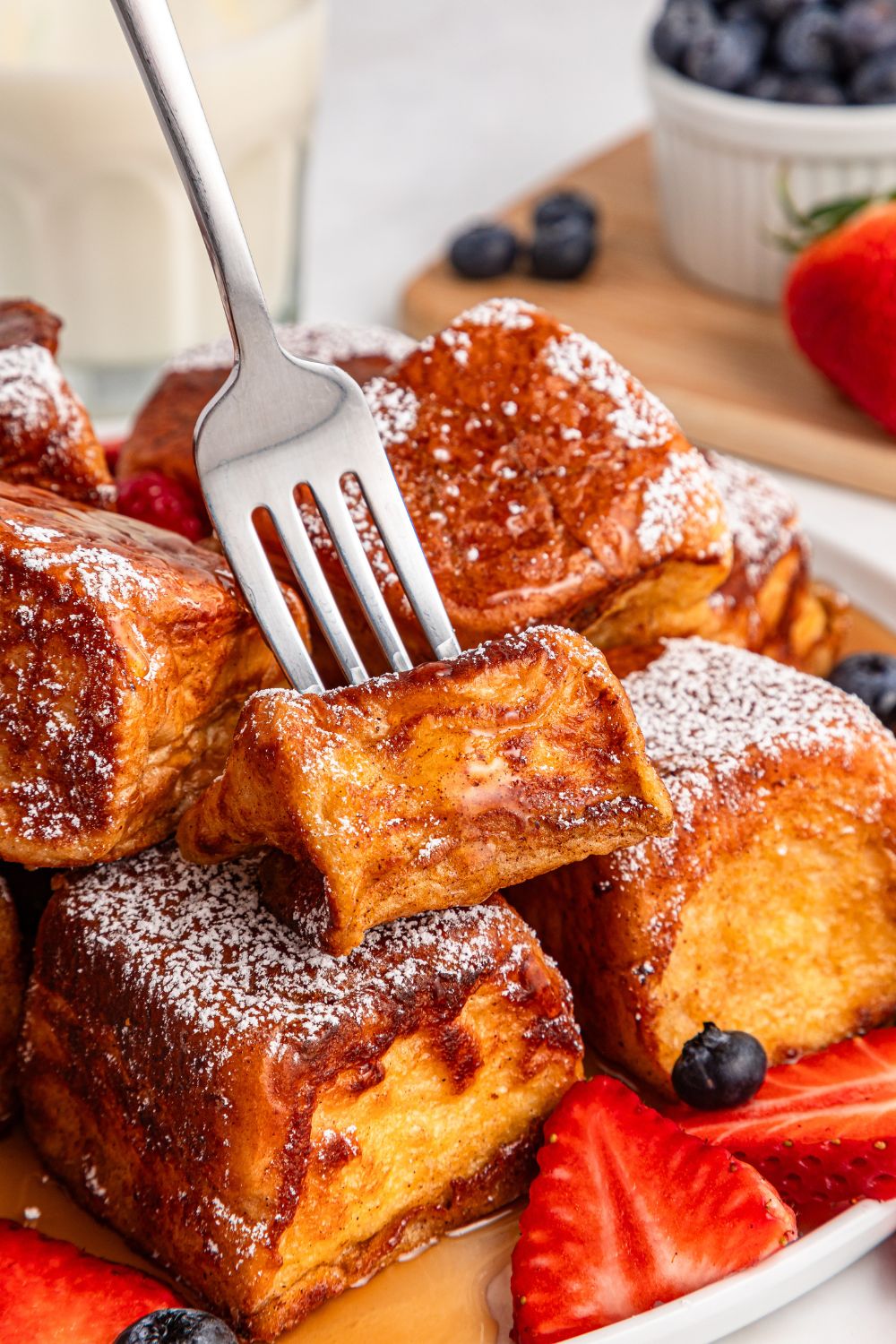 fork poking into a bite of Hawaiian Roll French Toast on plate with strawberries and blueberries 