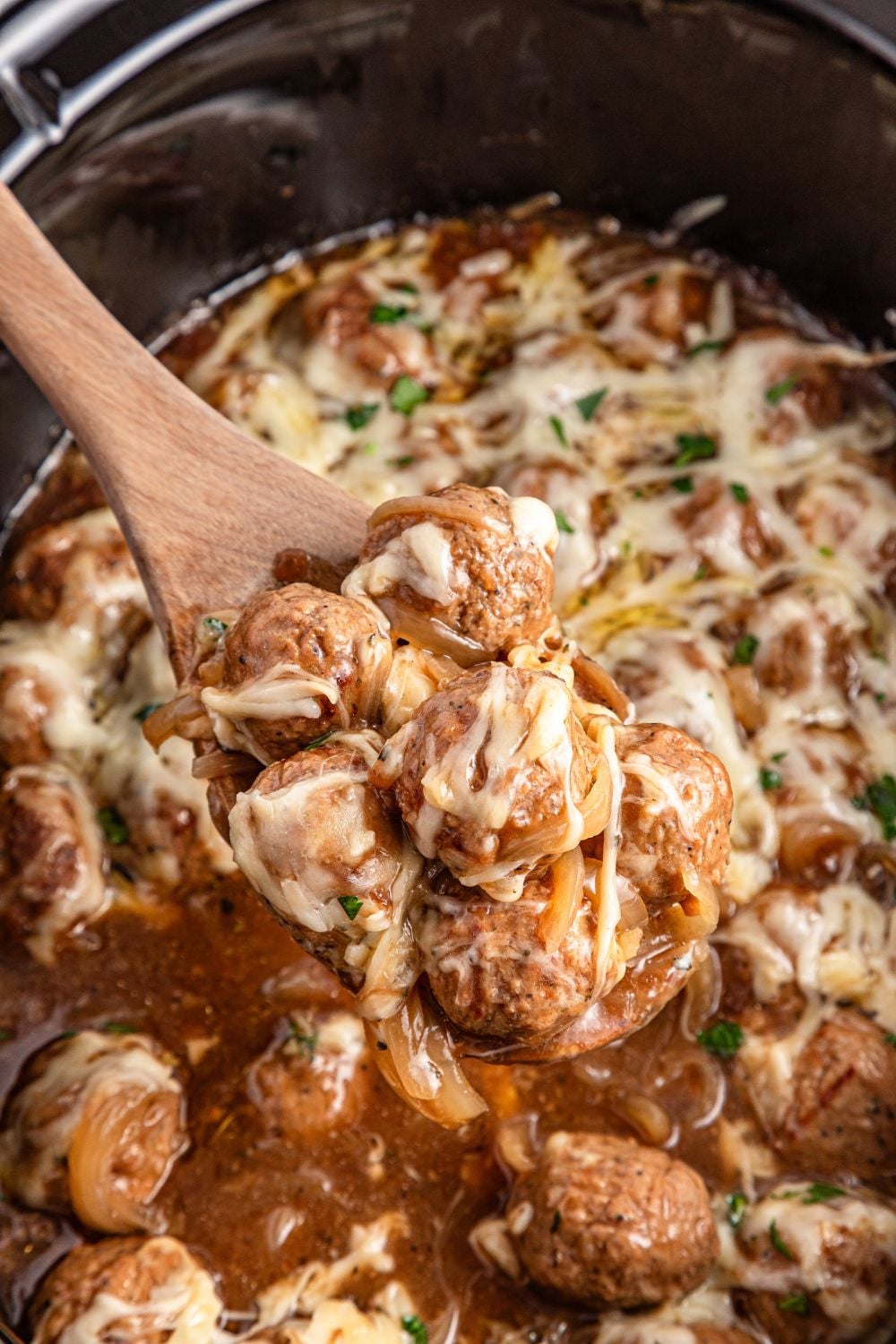 Crock Pot French Onion Meatballs in a slow cooker getting some scooped out with a wooden spoon