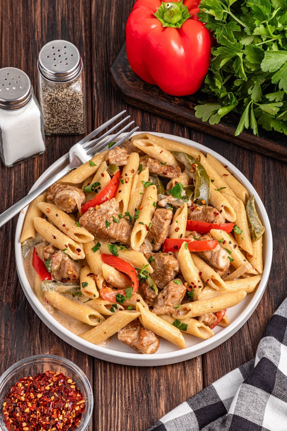 Rasta Pasta on a plate with a fork on side, fresh produce, and salt and pepper shaker on table by the plate