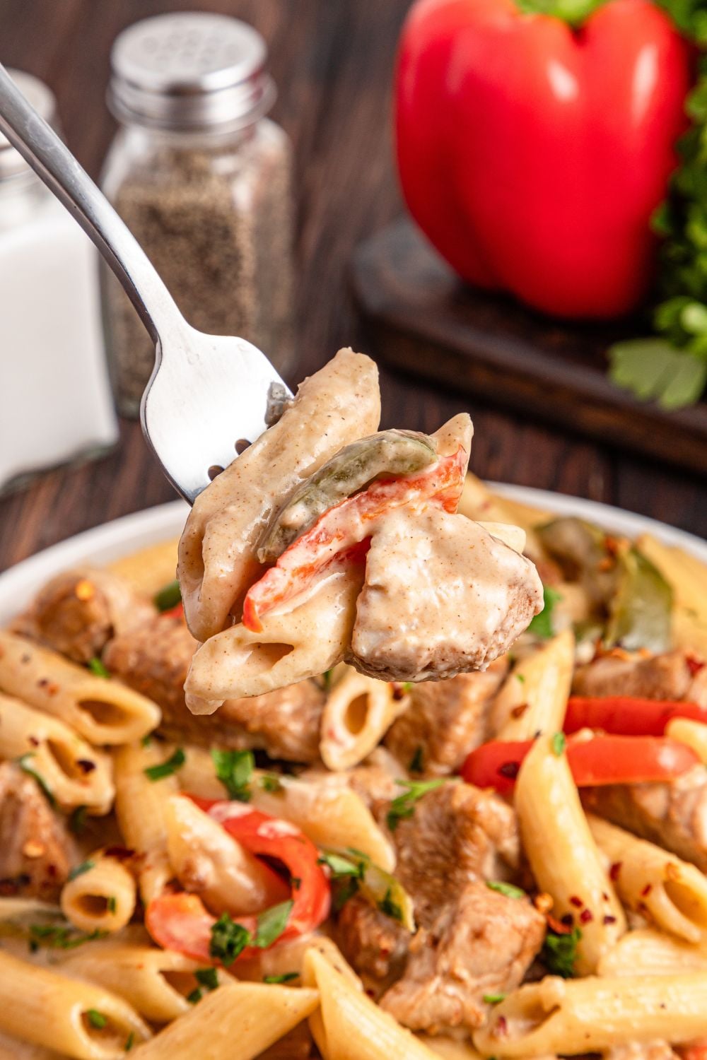 fork with a bite of rasta pasta on it, sitting above a bowl of pasta on table