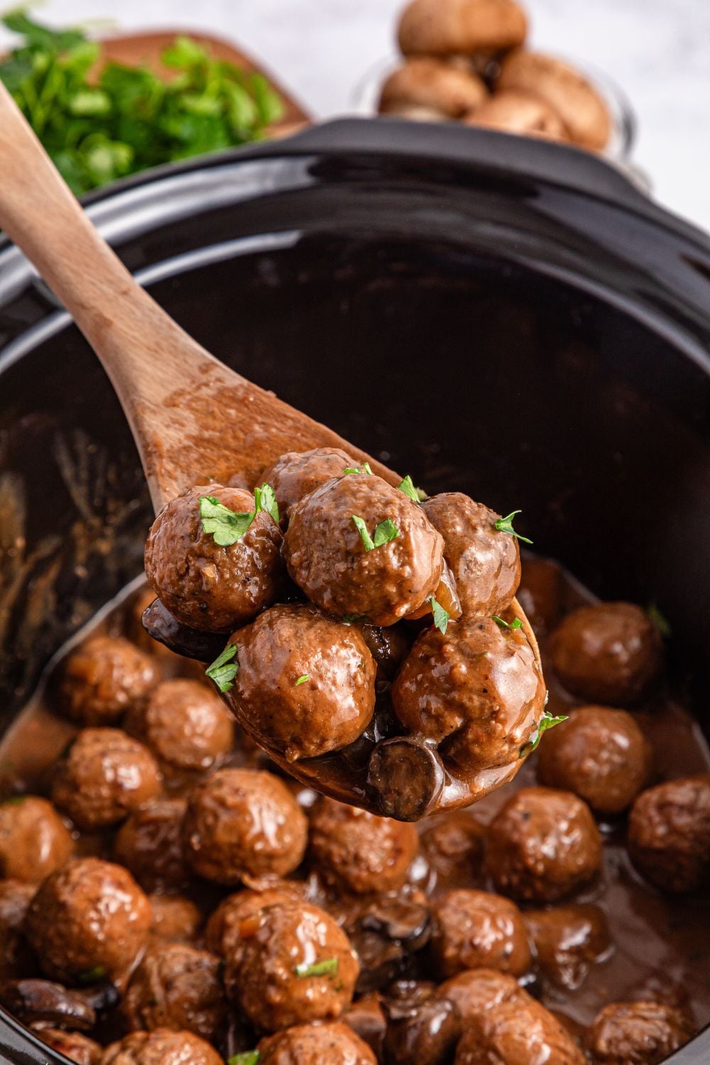 Crock Pot Salisbury Steak Meatballs in a crockpot on table with a wooden spoon with some meatballs being lifted out of the crockpot