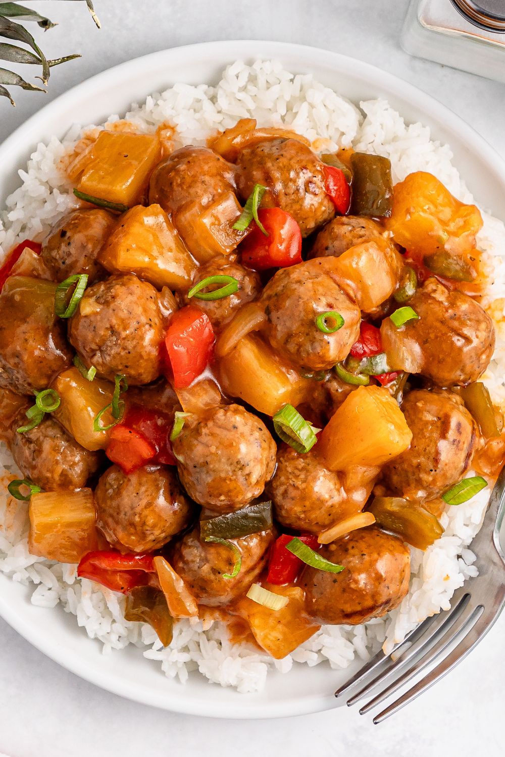 Sweet And Sour Meatballs over a bed of rice on plate on table