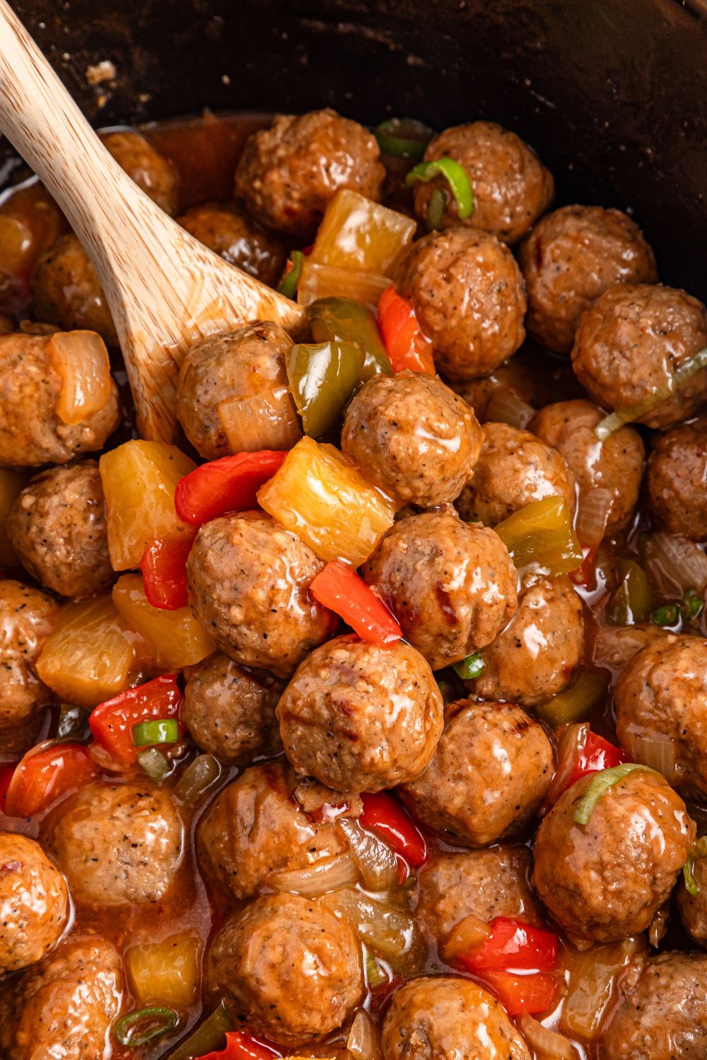 meatballs in slow cooker with a wooden spoon scooping out